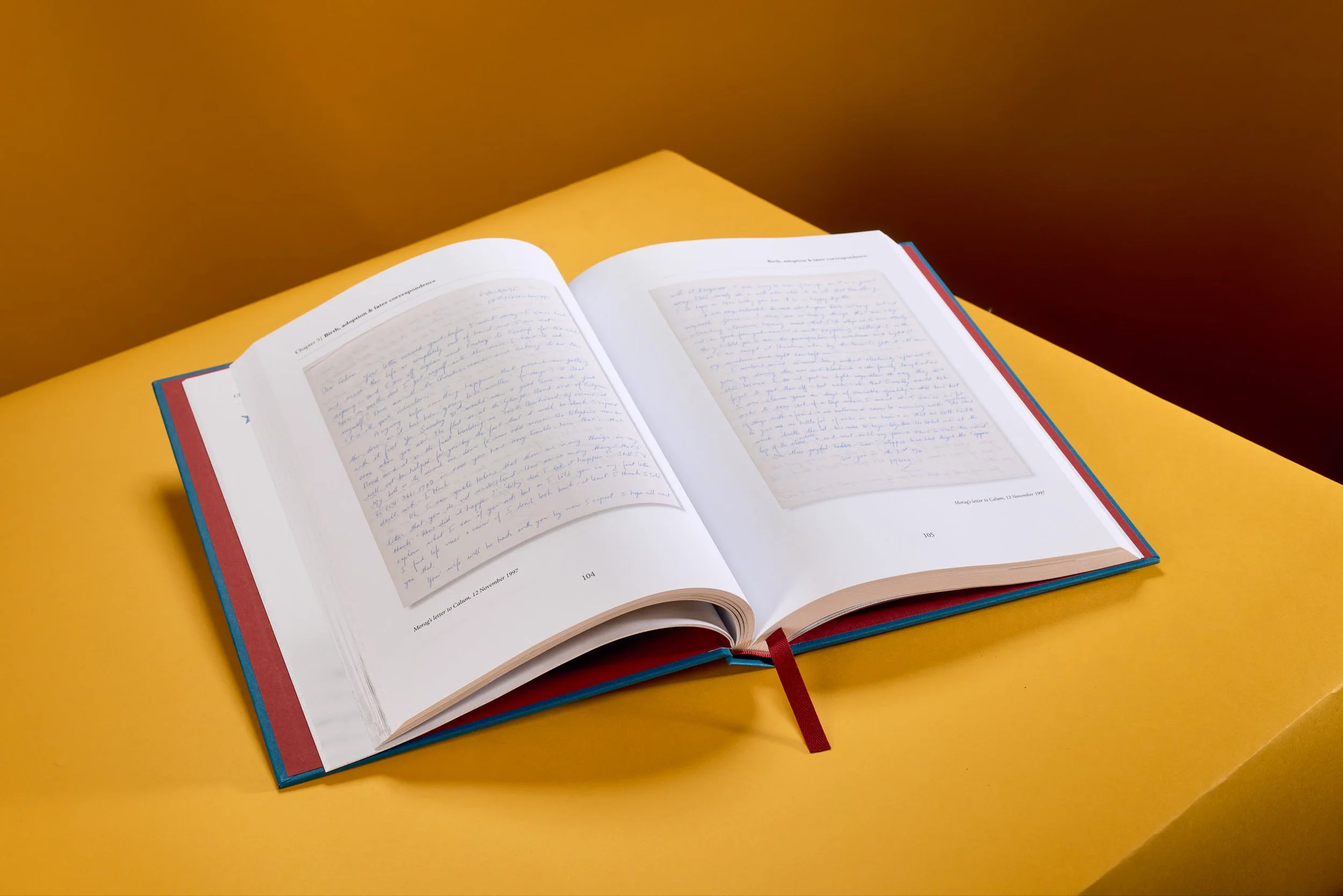 An open book with handwritten pages resting on a yellow surface against a brown background.