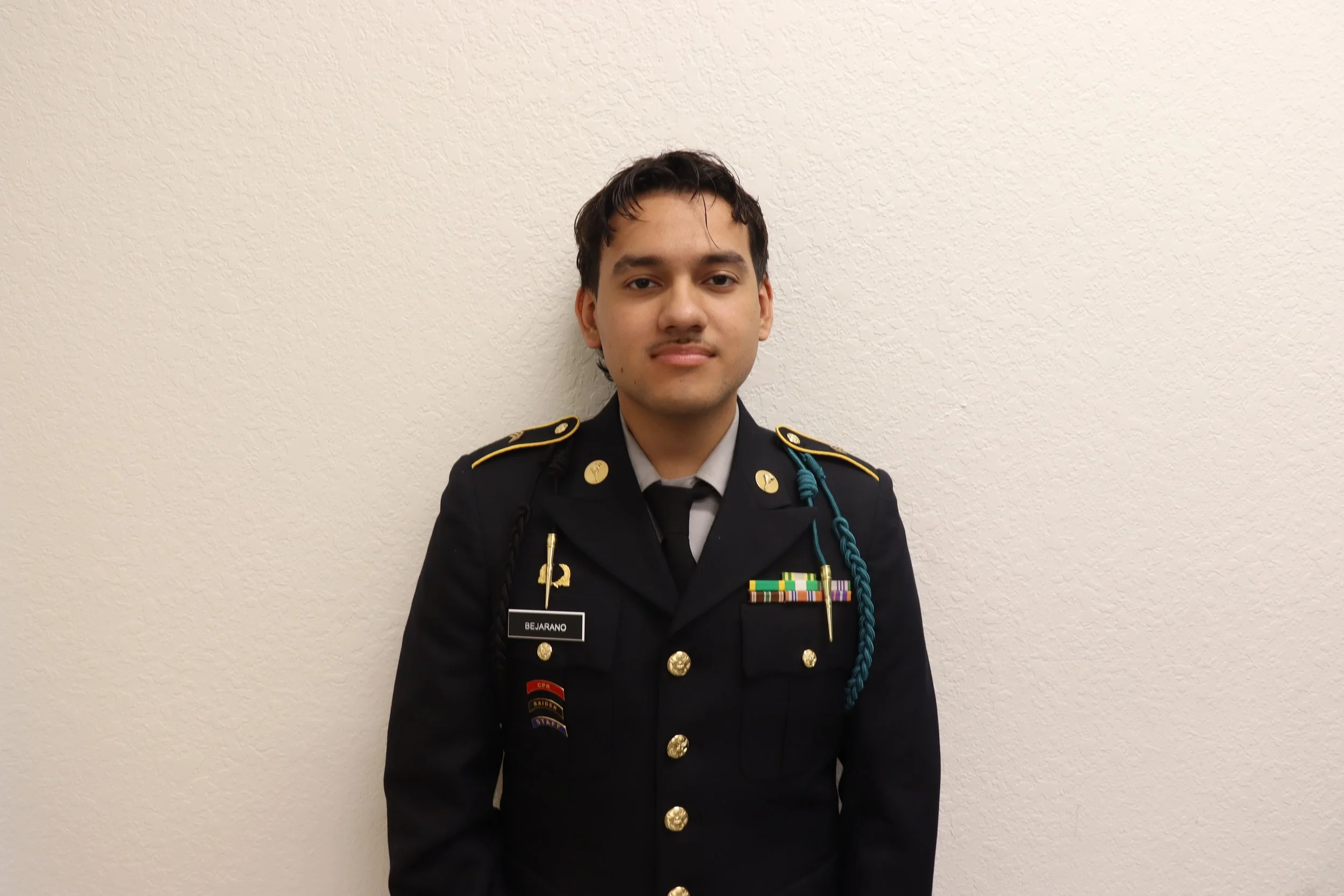 Young man in formal military uniform standing against a plain white wall.