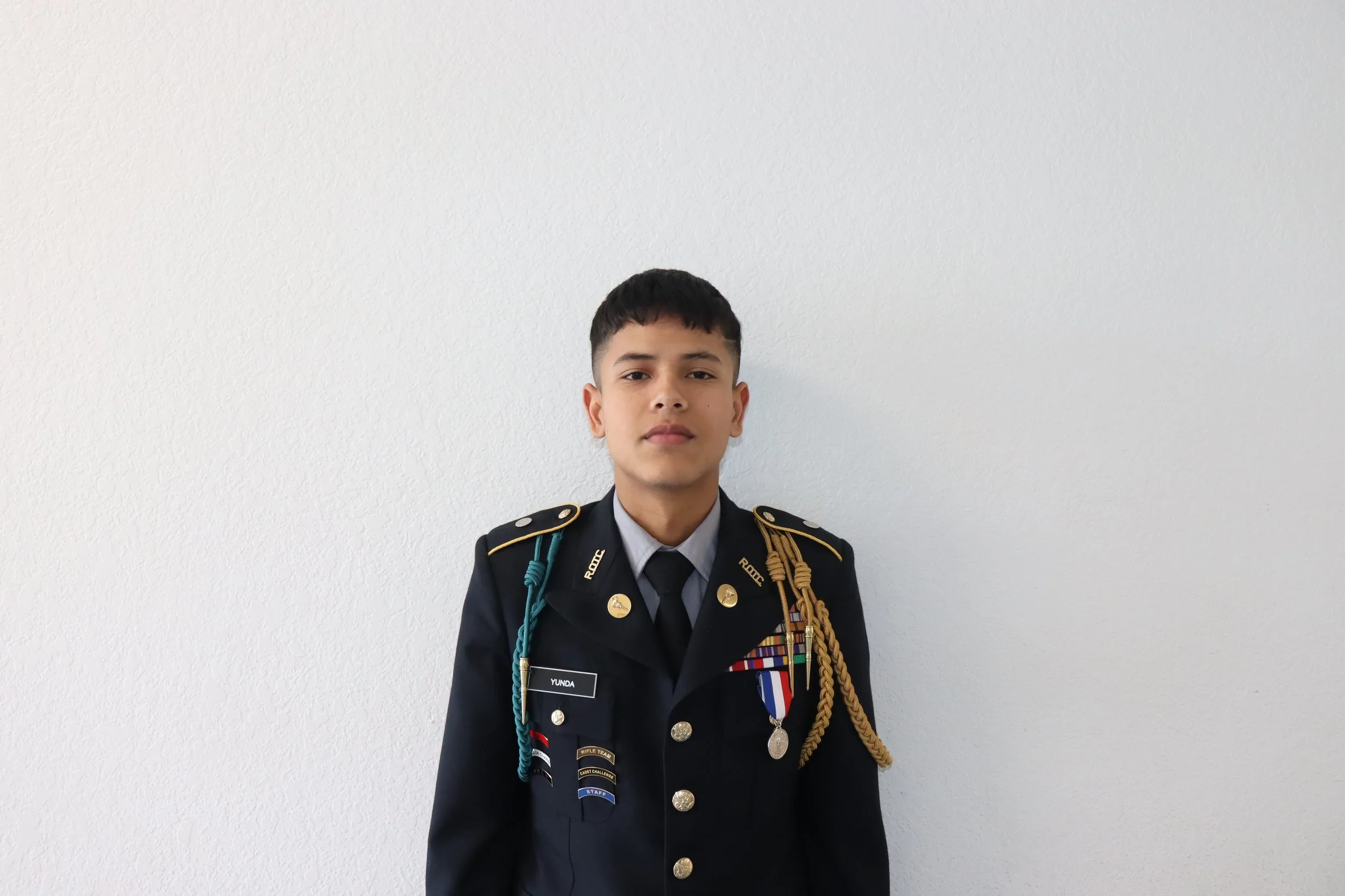 Young man in a ceremonial military dress uniform standing against a plain white wall.