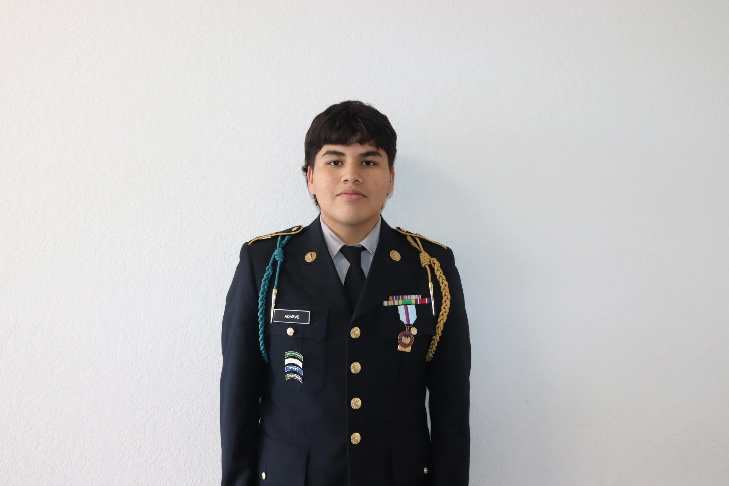Young man in a formal military uniform standing against a plain white wall.