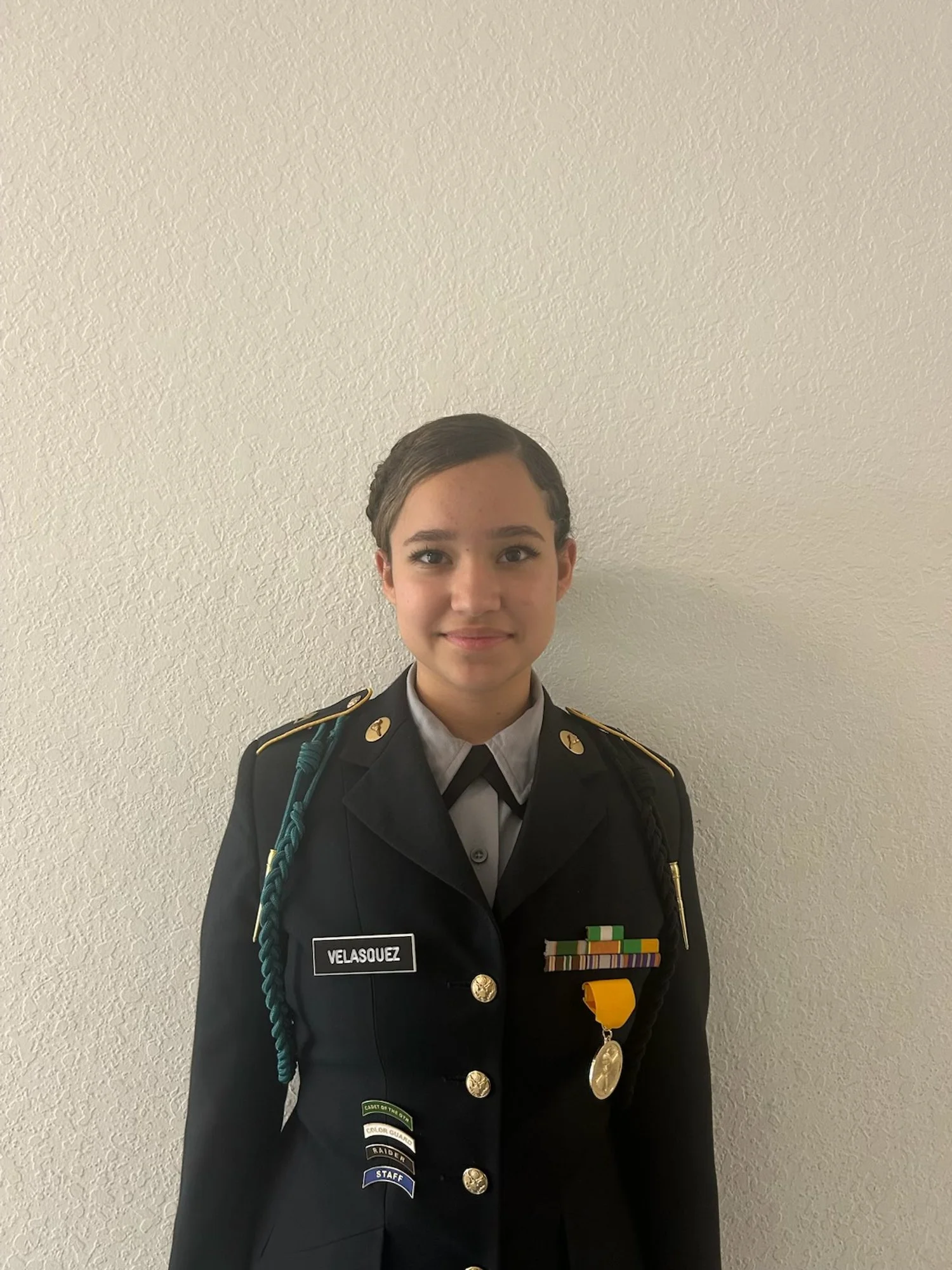 Young woman in military uniform standing against a white wall.