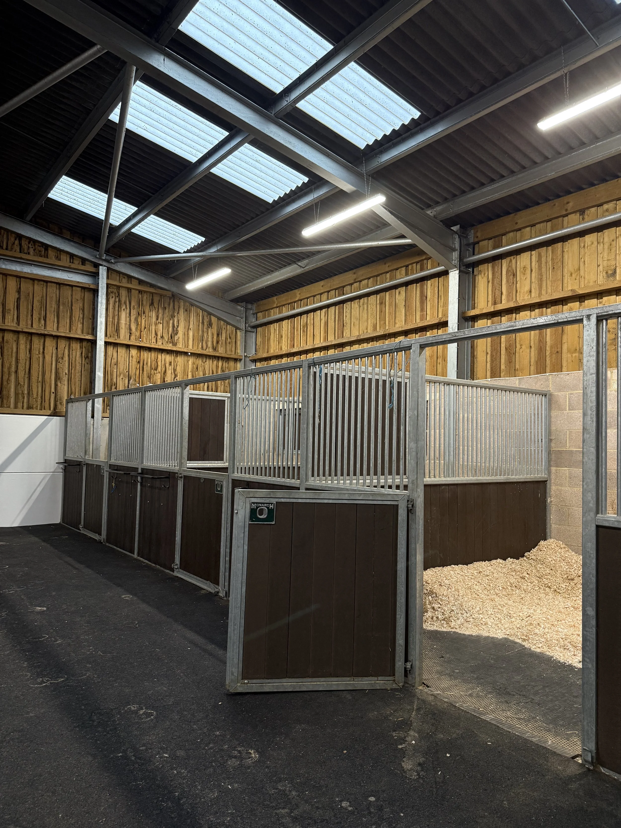 Indoor horse stall with wooden walls, metal bars, and a pile of bedding on the floor.