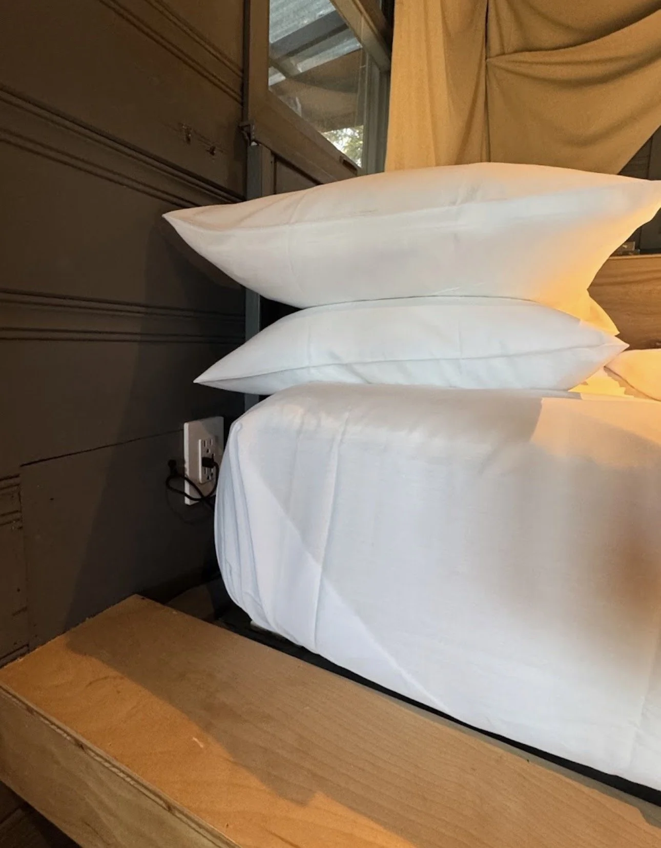 Stacked white pillows on a bed in a room with wood and dark colored panels.