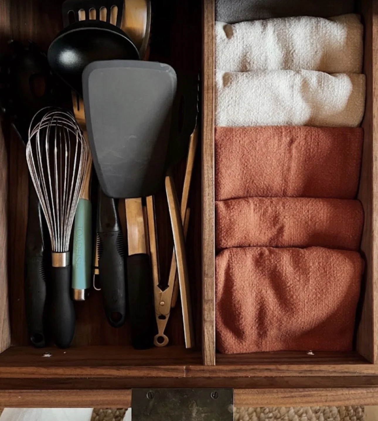 Kitchen drawer with utensils on the left side and folded cloth towels on the right side.