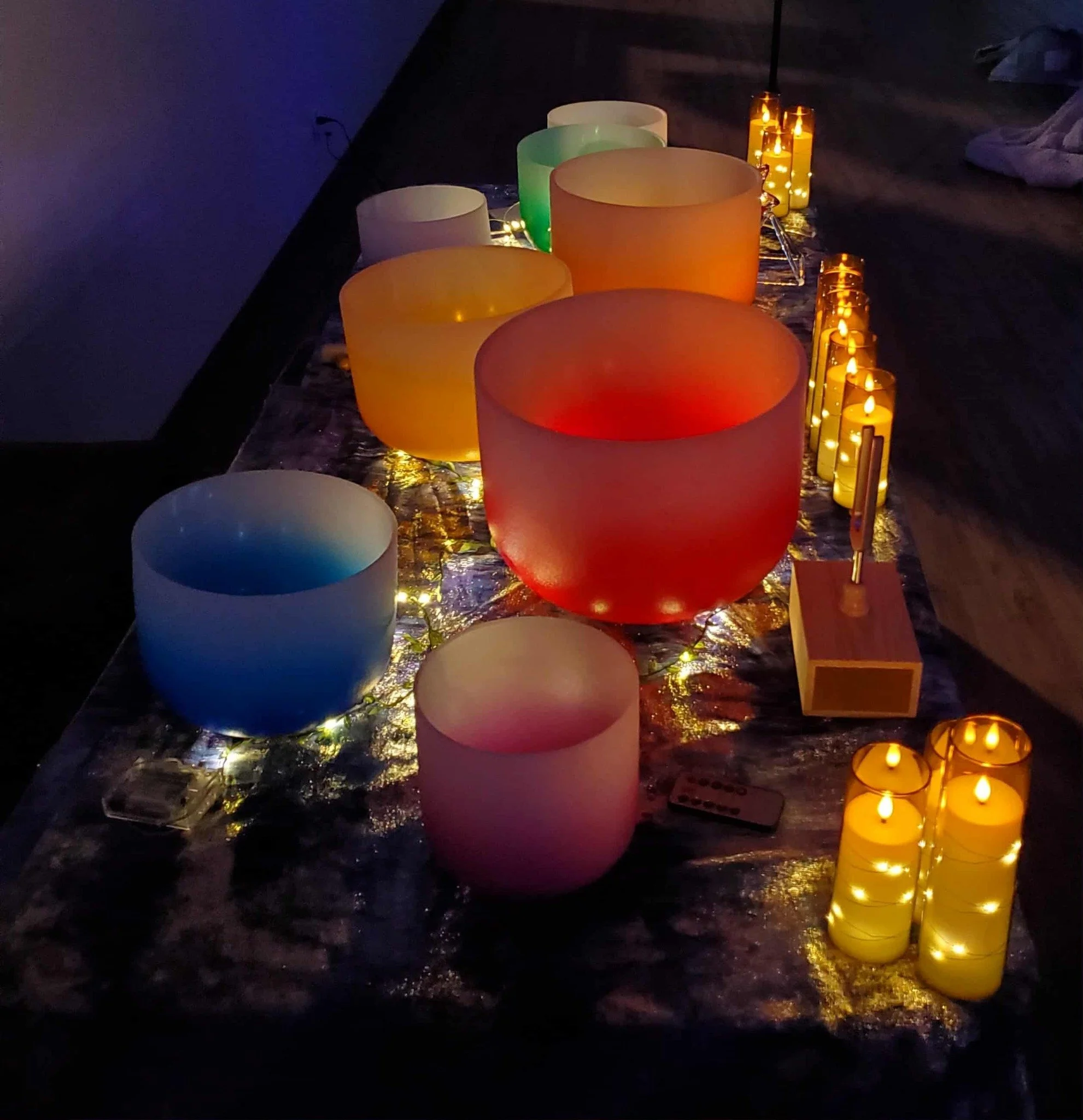 Colorful glass bowls and candles arranged on a table with string lights.