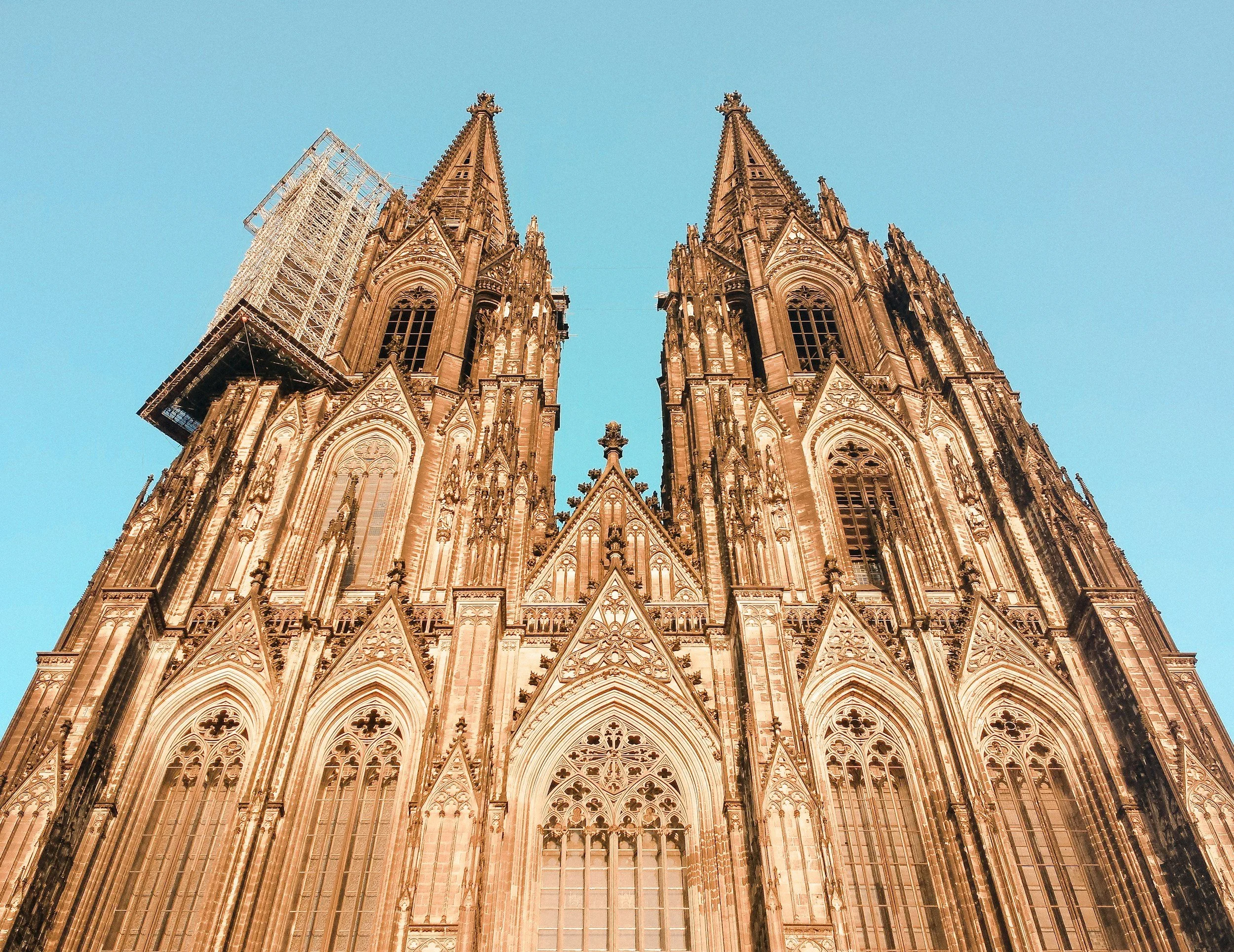 Gothic cathedral with twin spires and ornate architectural details, viewed from below against a clear blue sky.