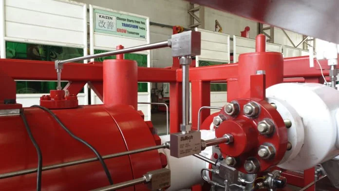 Industrial machinery with red and white components, pipes, and bolts, situated in a factory setting.