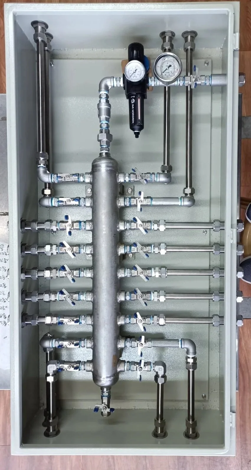 An industrial plumbing manifold with multiple valves, pipes, and two pressure gauges inside a metal box.