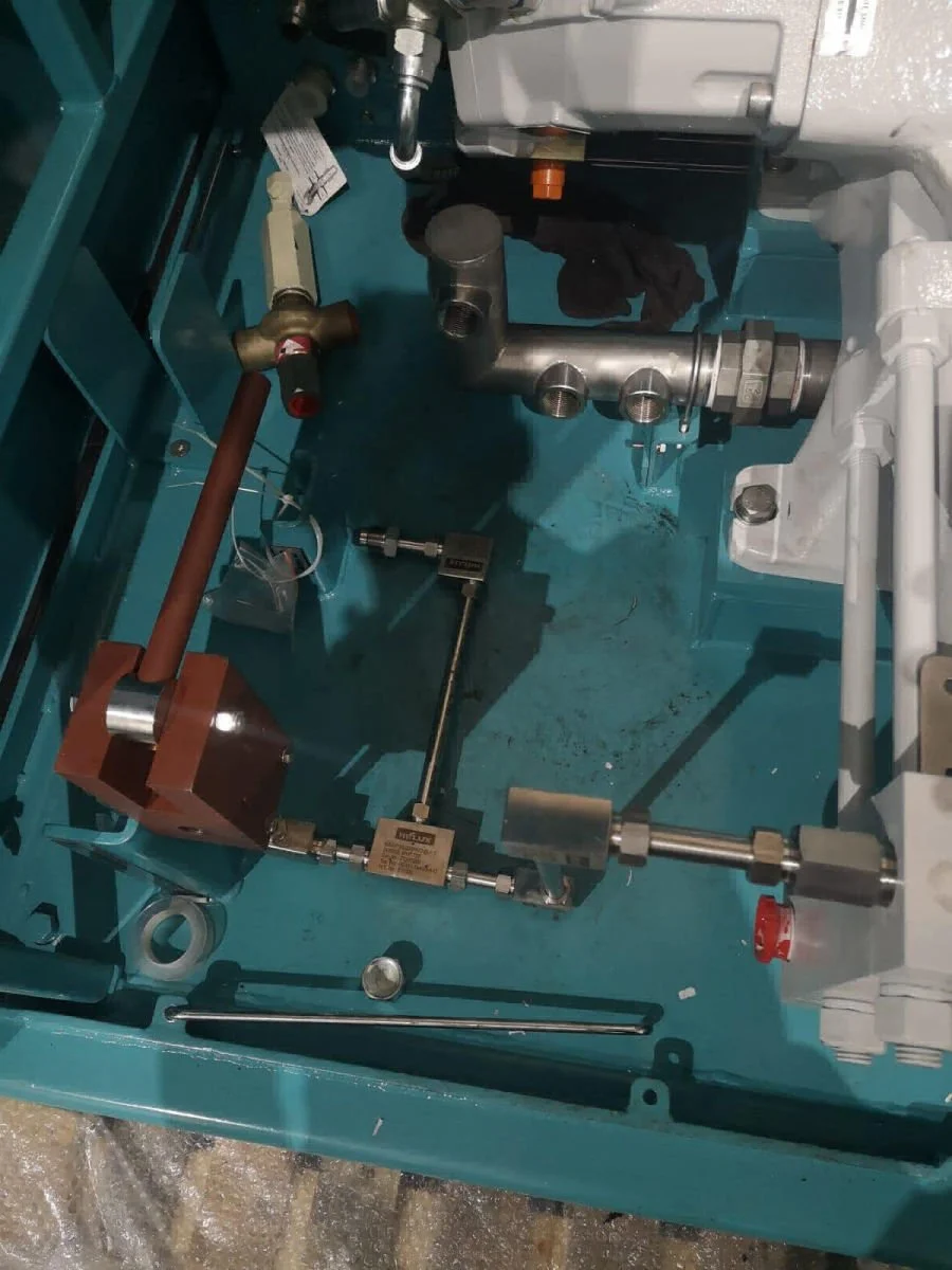 Close-up of plumbing and mechanical components inside an industrial or manufacturing machine, including pipes, fittings, and metal parts.