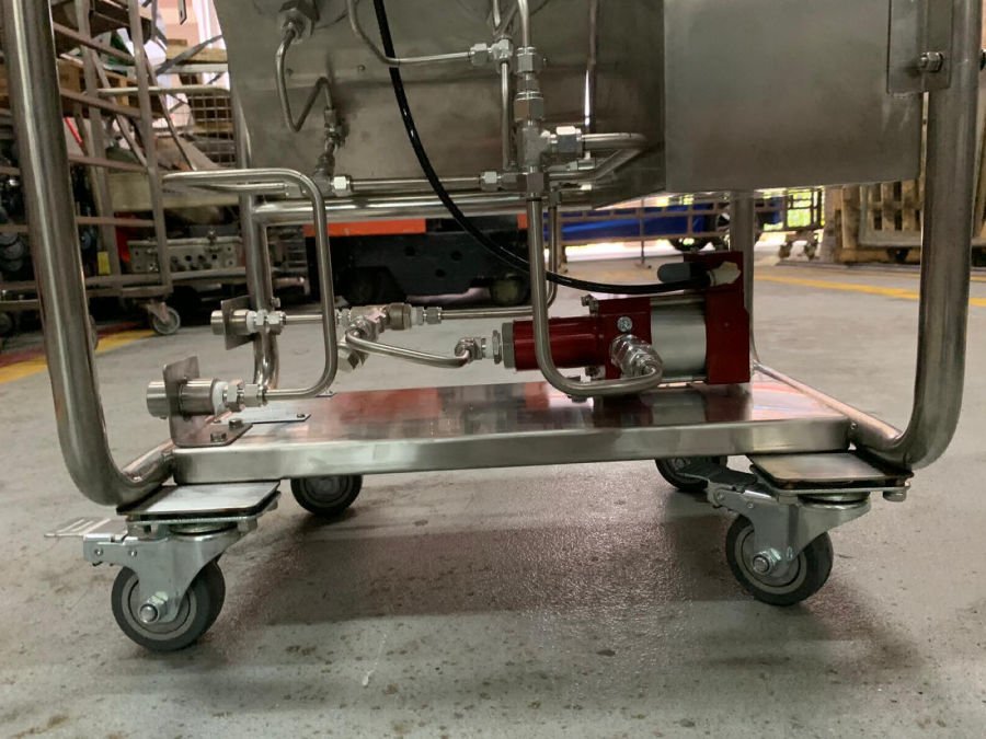 Metal equipment and piping on a stainless steel mobile cart with wheels in an industrial or warehouse setting.