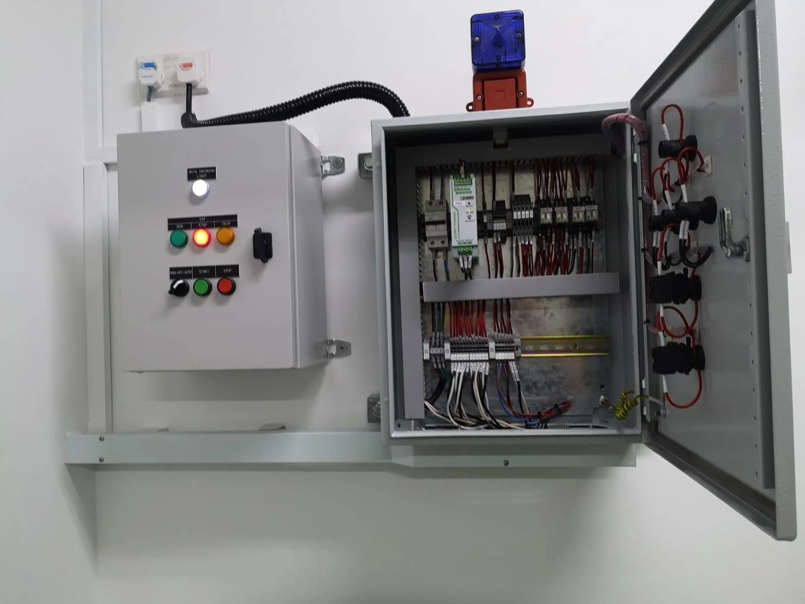 Electrical control panel with inner wiring, switches, and relays, mounted on a wall with a separate smaller control box connected to the main panel.