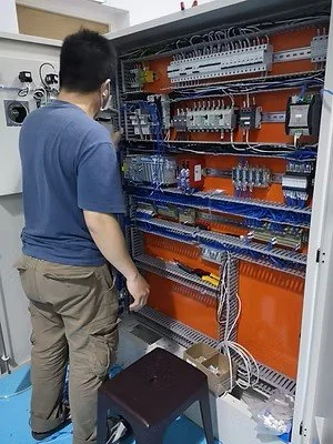 A man working on an electrical control panel with organized wiring and components inside a metal enclosure.