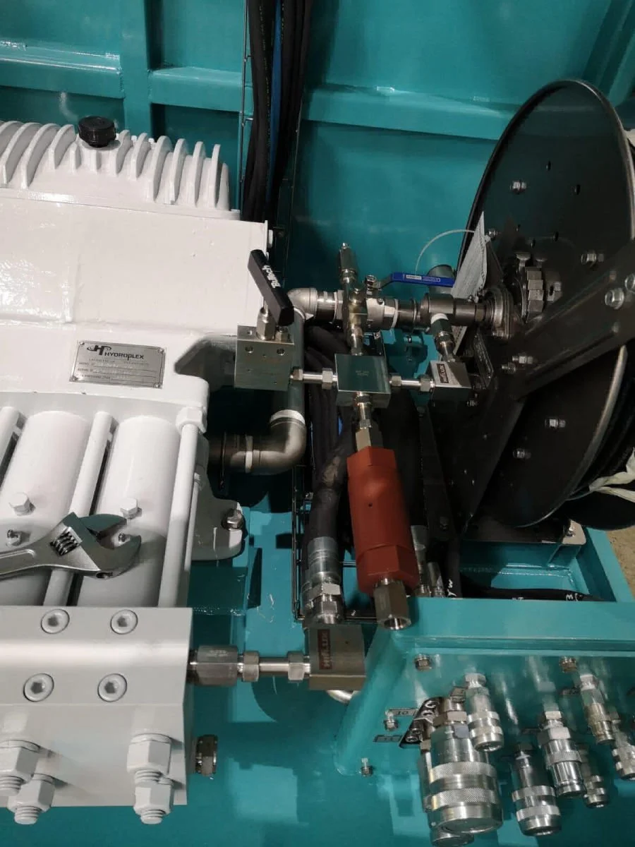 Close-up of industrial machinery with pipes, fittings, valves, and a white component on a teal-colored surface.