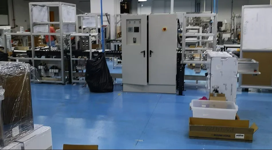 Industrial manufacturing or assembly workspace with machinery, tools, and storage containers.