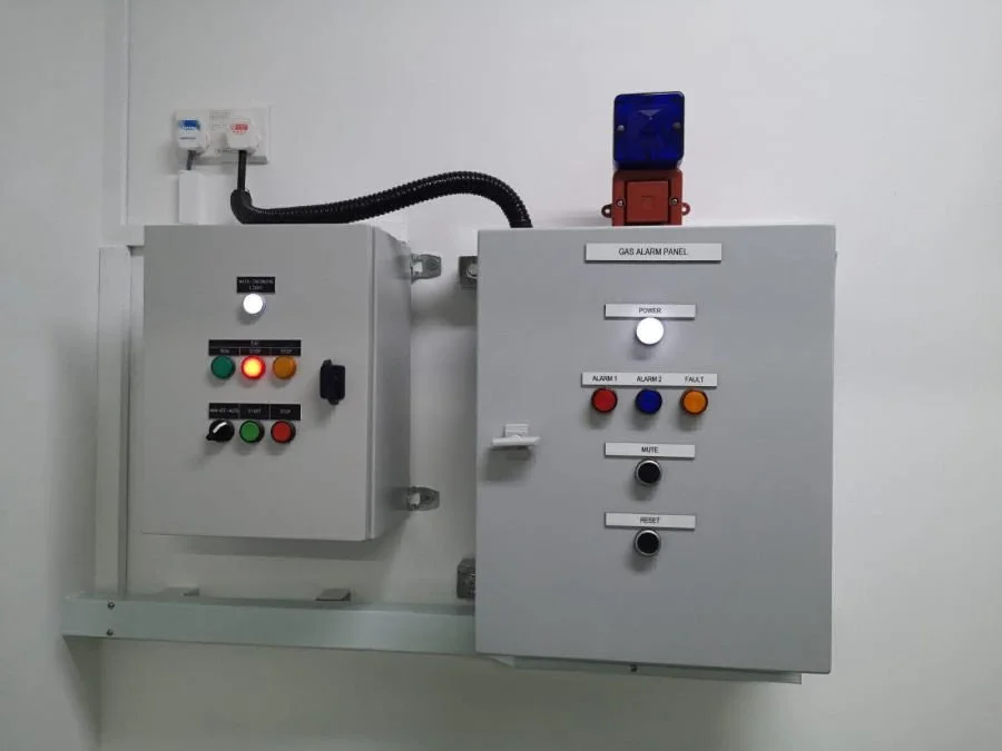 Electrical panel with gas alarm system, warning lights, buttons, and switches mounted on a white wall.