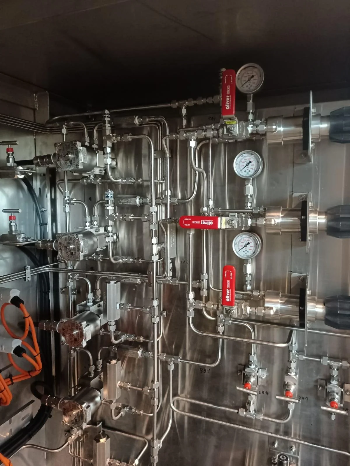 Close-up view of a stainless steel industrial piping system with pressure gauges, valves, and fittings.