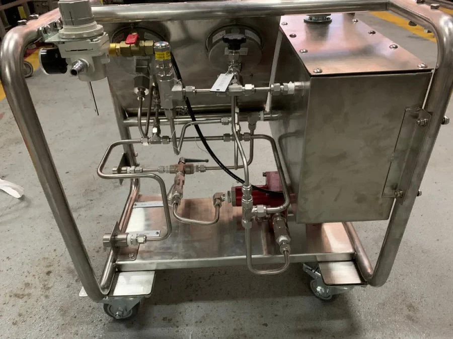 Stainless steel industrial equipment with pipes, valves, and gauges on a wheeled cart.