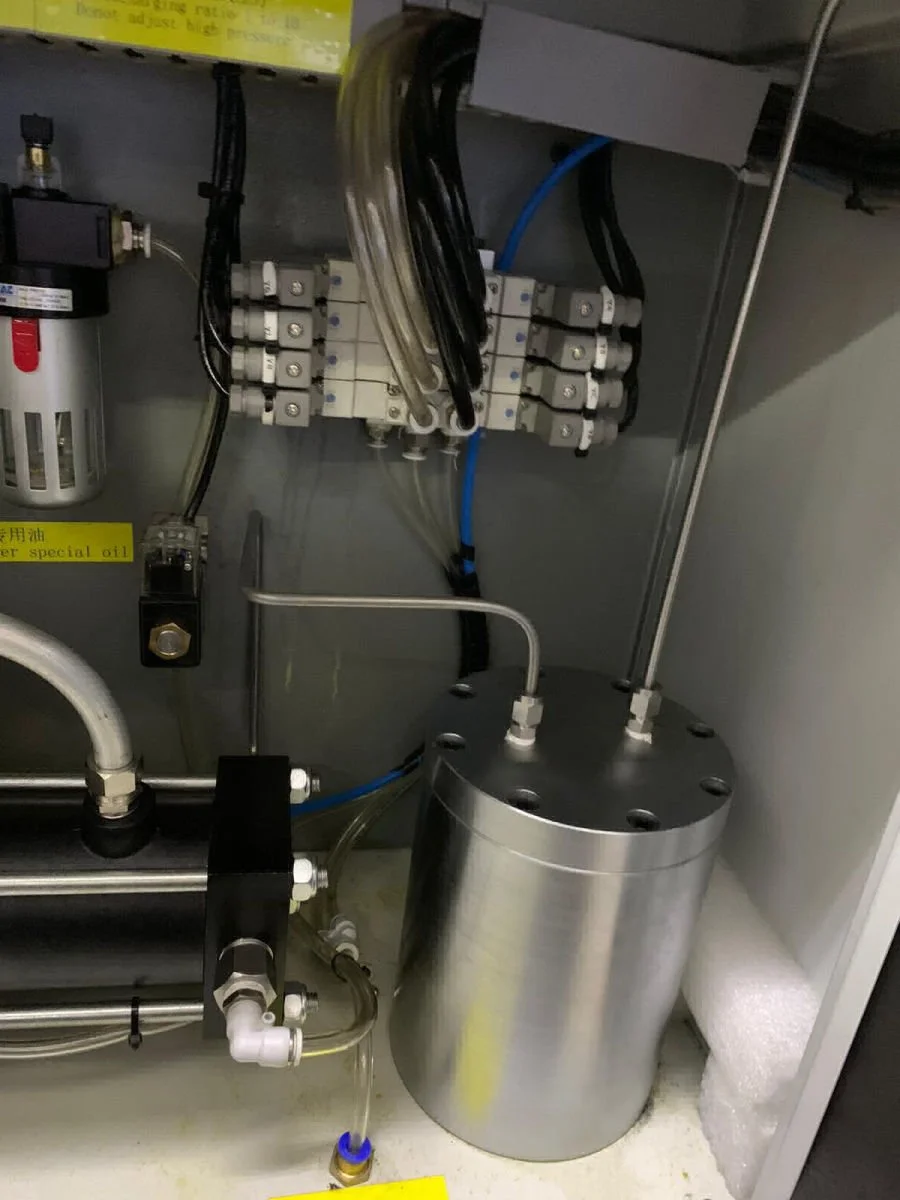 Close-up of an industrial machine interior with pipes, wires, and metal components, including a cylindrical stainless steel tank and a filter system.