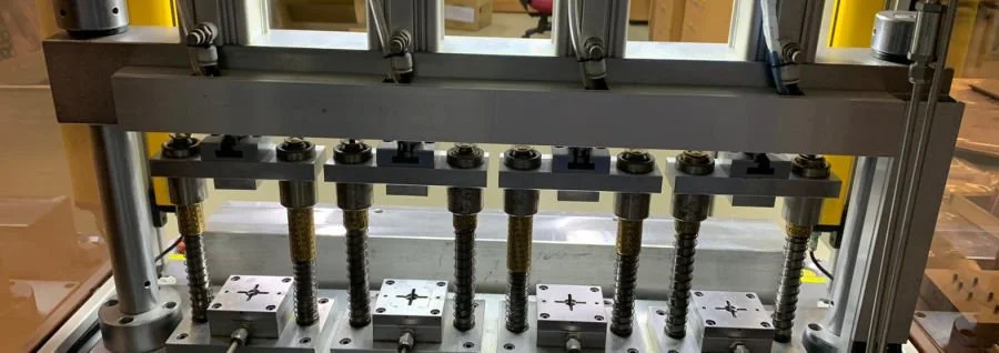 Close-up of a machine with evenly spaced metal screws and fixtures inside a factory or workshop.