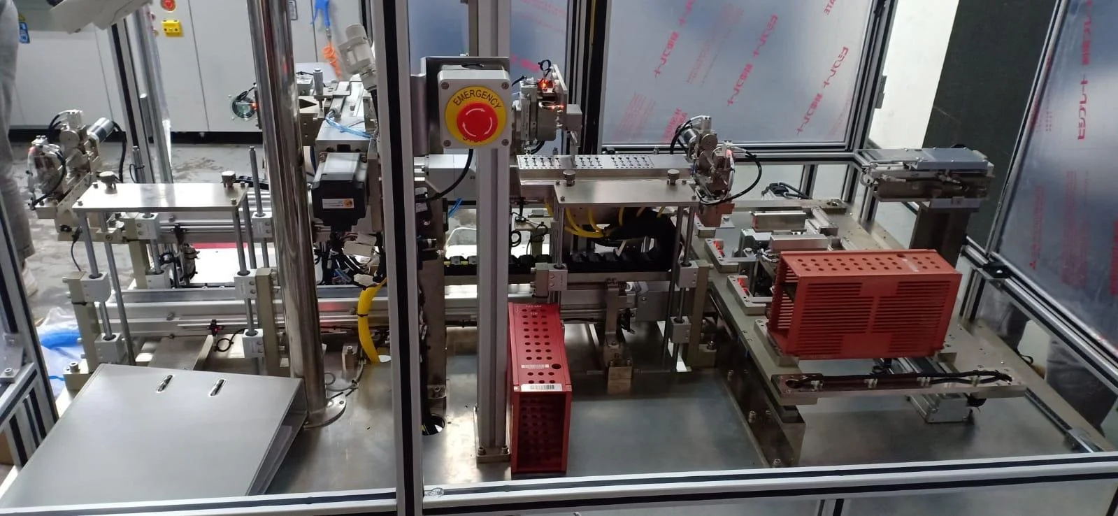 Industrial machinery setup with metal components, wiring, and a red emergency stop button in a manufacturing or laboratory environment.