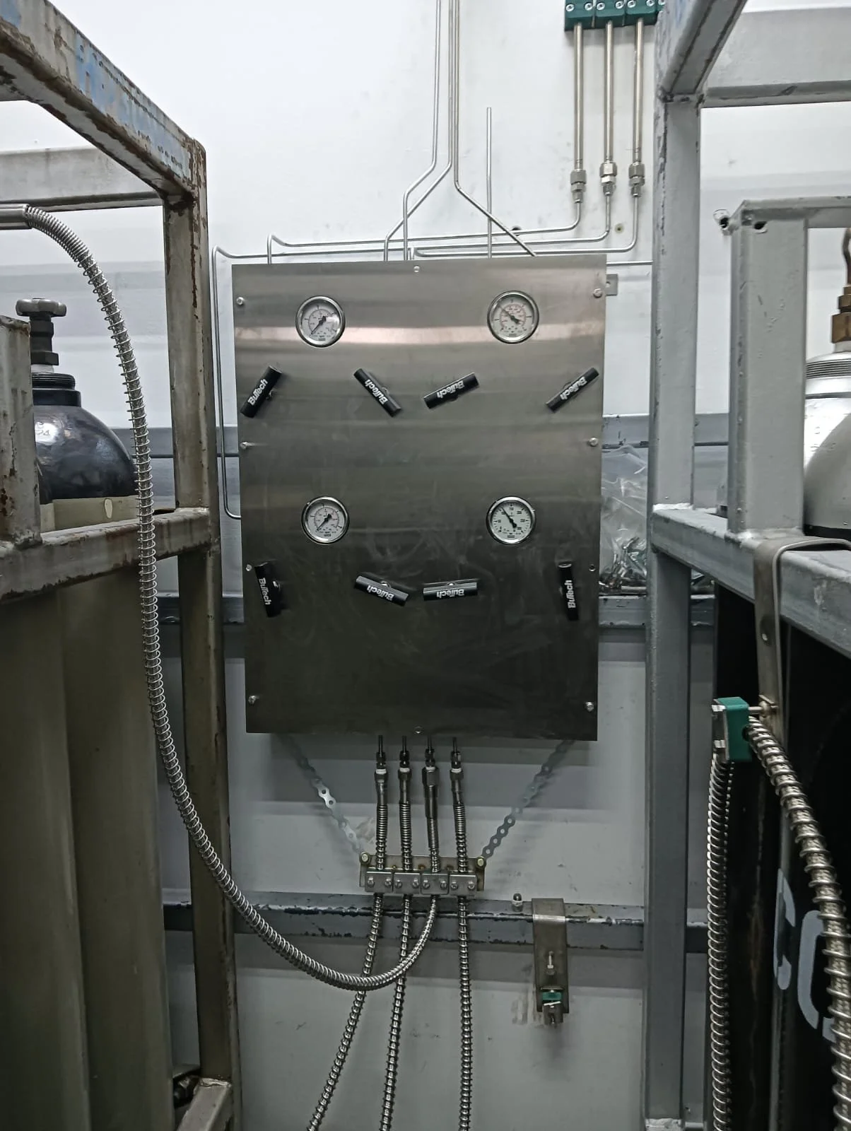 Industrial machine panel with four pressure gauges and several control valves and pipes connected to it.