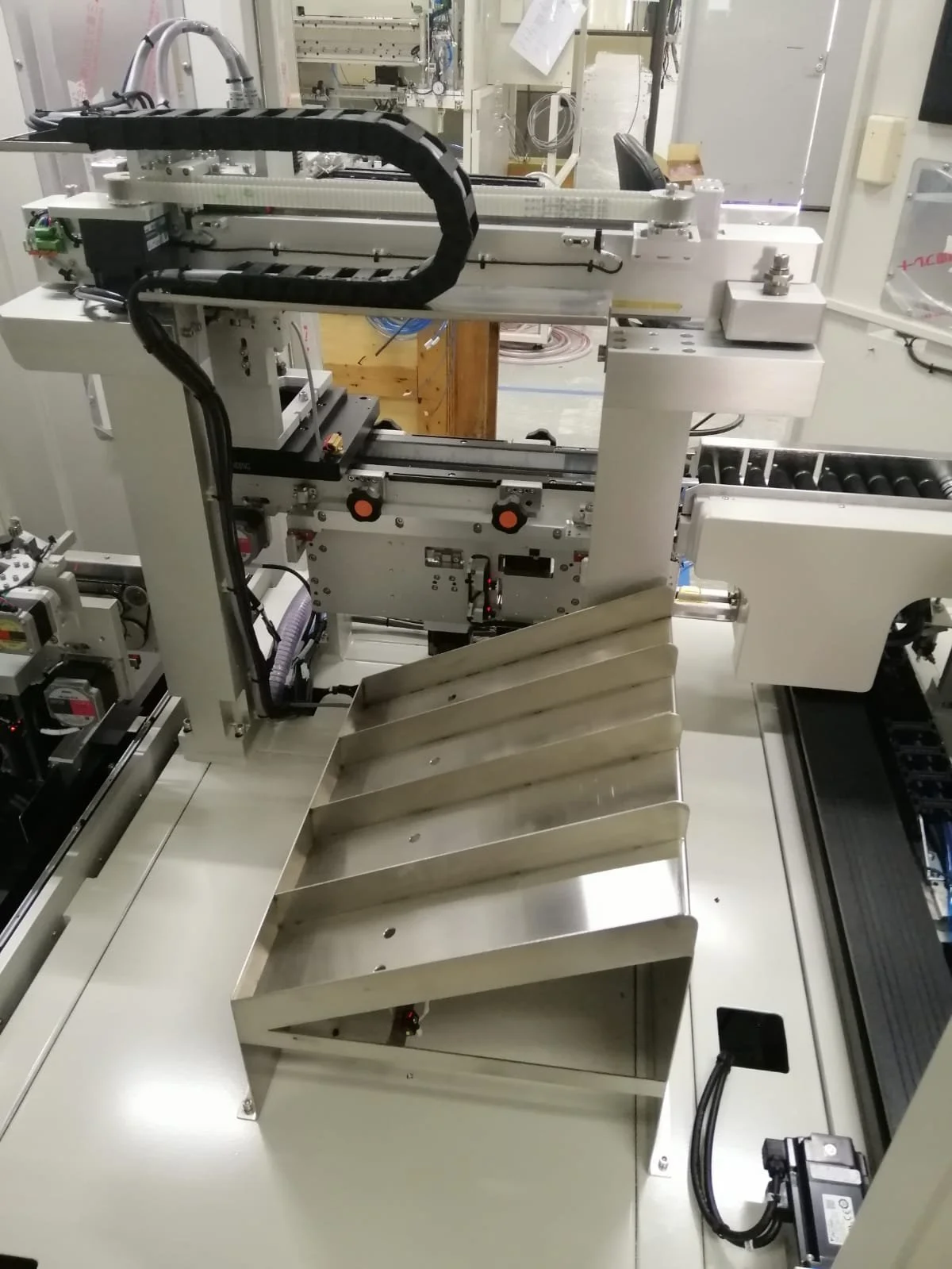 A complex piece of industrial machinery with metal components, wiring, and rollers, situated in a laboratory or manufacturing setting.