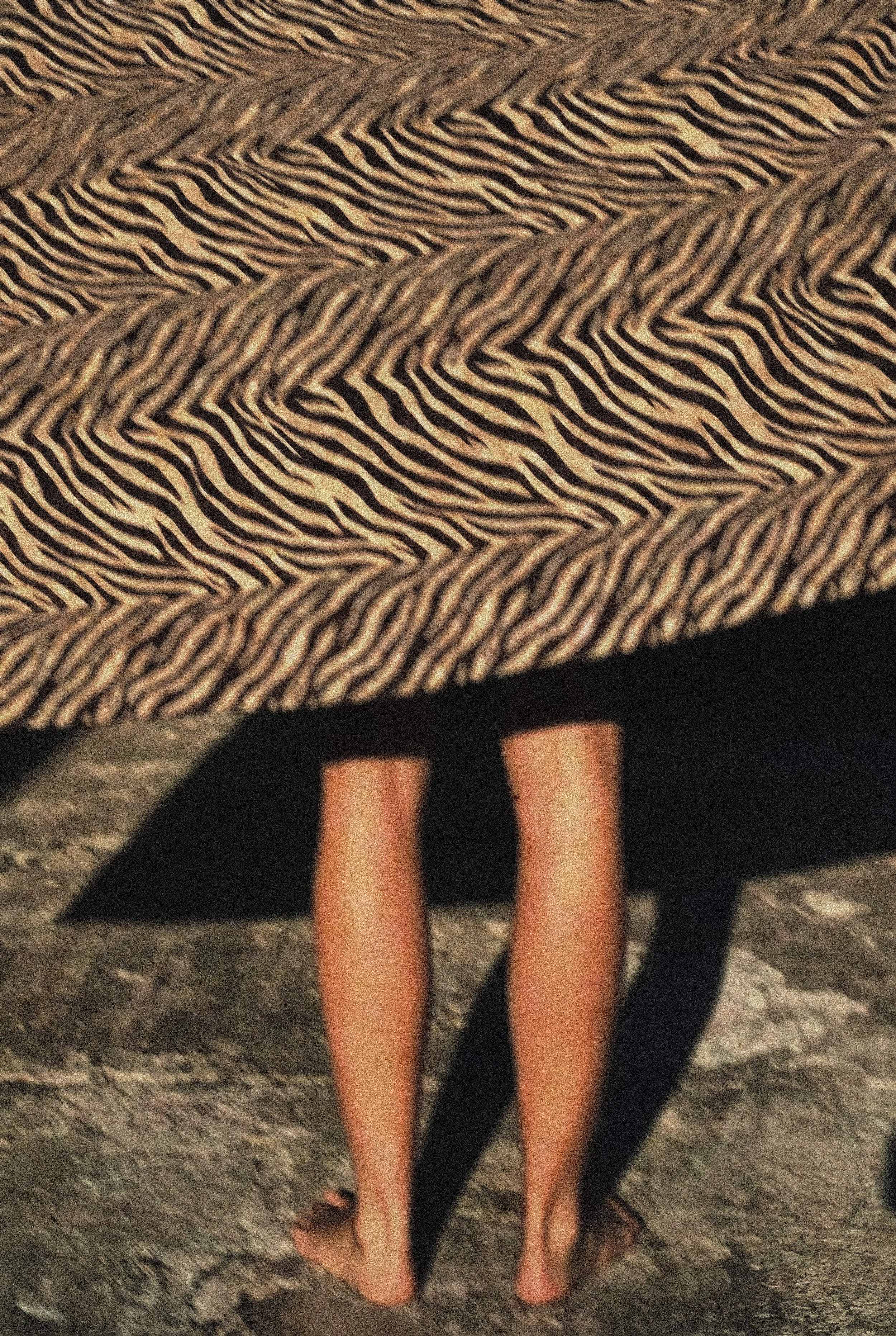 One woman standing barefoot on rocky ground, partially covered by a black and white patterned fabric.