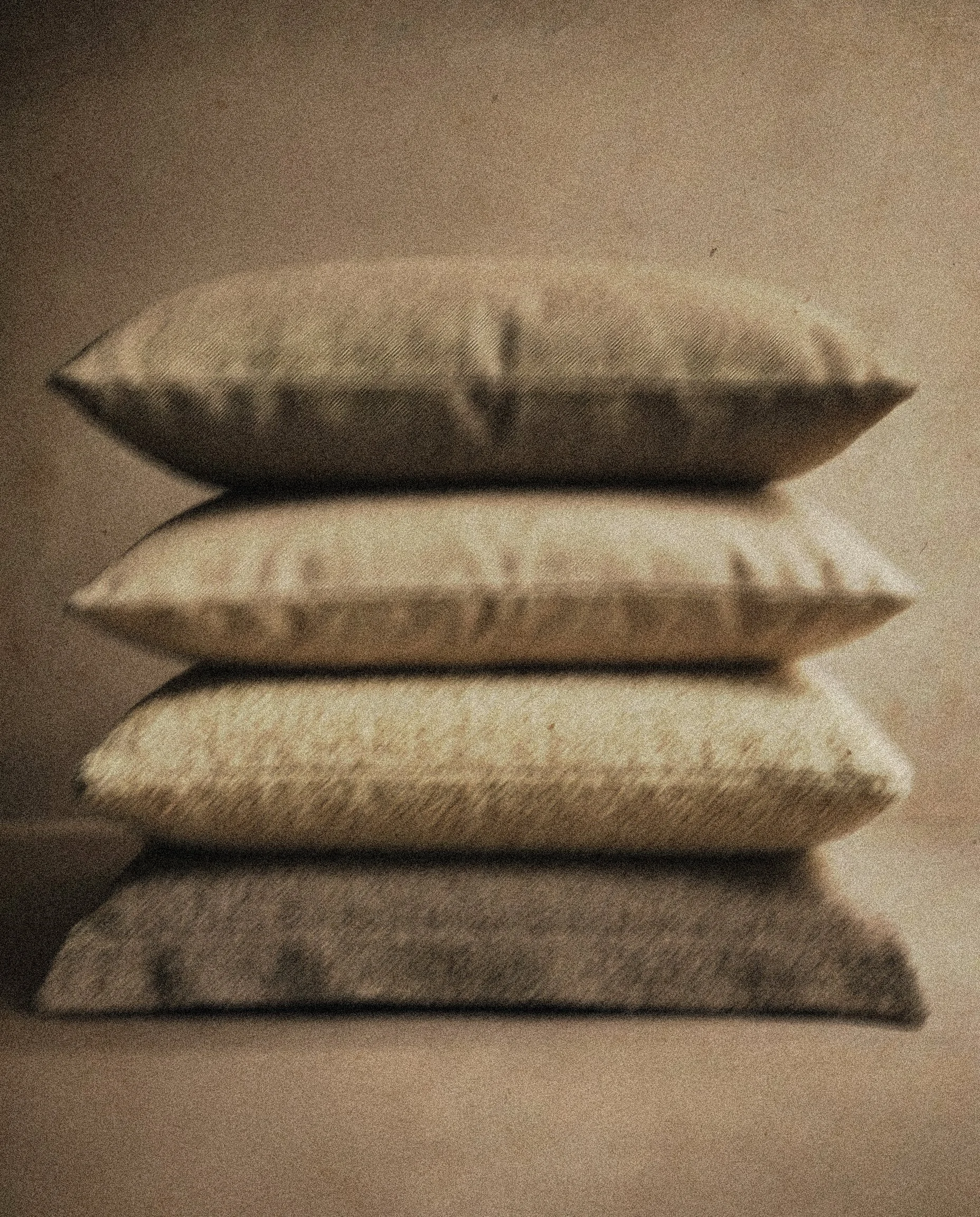 Close-up of a stack of four pillows with soft textured surfaces, resting on a flat surface.