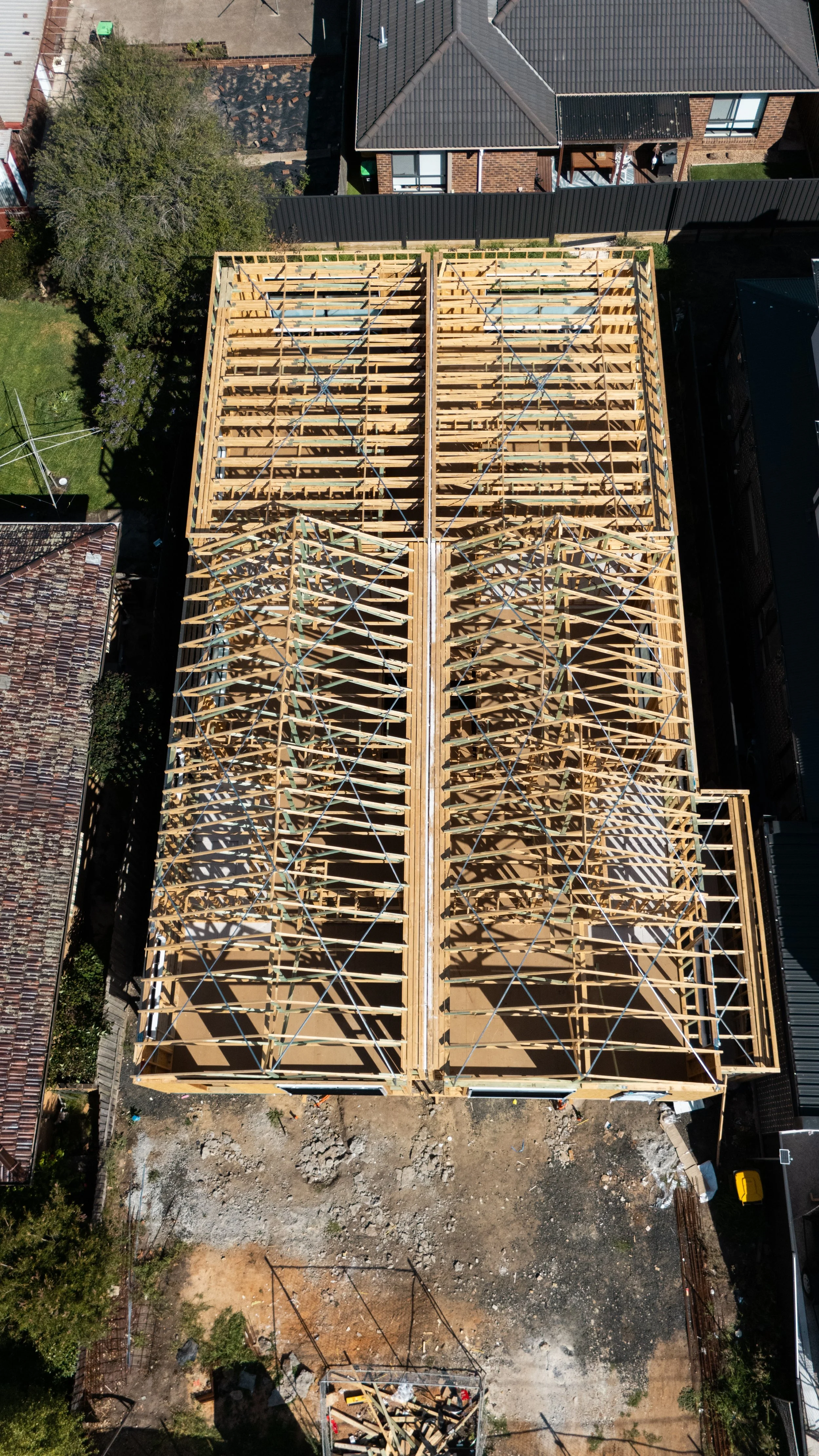 Aerial view of a house under construction with exposed wooden framing and roof trusses. Construction made by Provue Built team