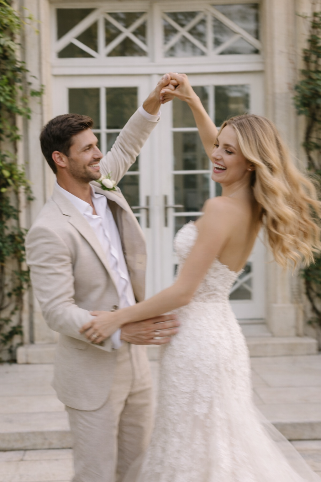 Ein glückliches Paar tanzt auf einer Hochzeit vor einem weißen Haus mit großen Fenstern, das Frau trägt ein langes weißes Brautkleid und Mann trägt einen hellen Anzug.