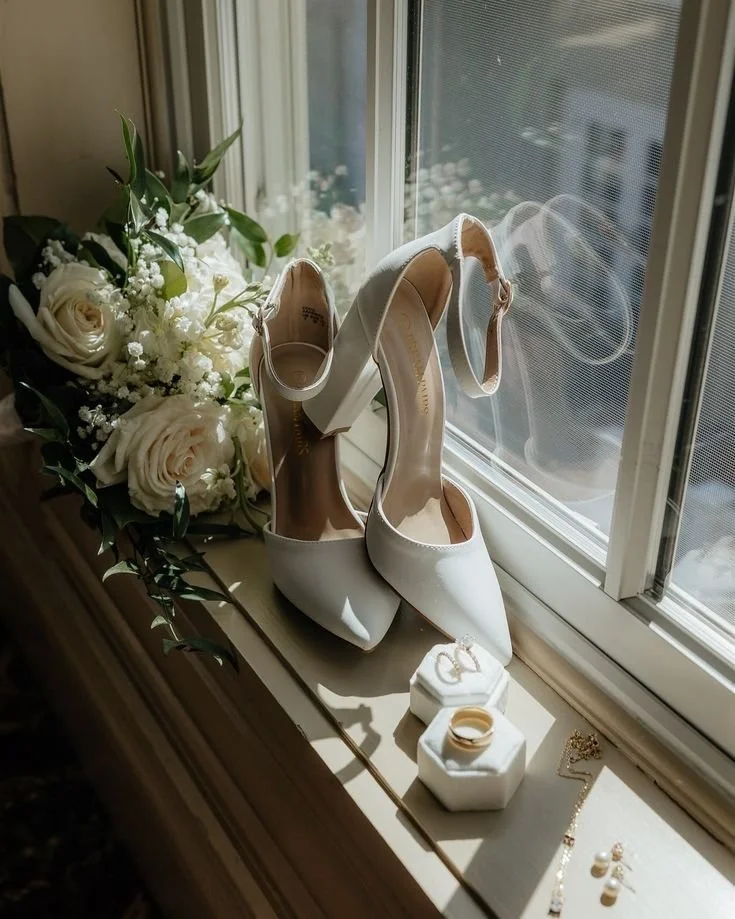 Hochzeitsschuhe, Brautstrauß, Eheringe und Schmuck auf einer Fensterbank.