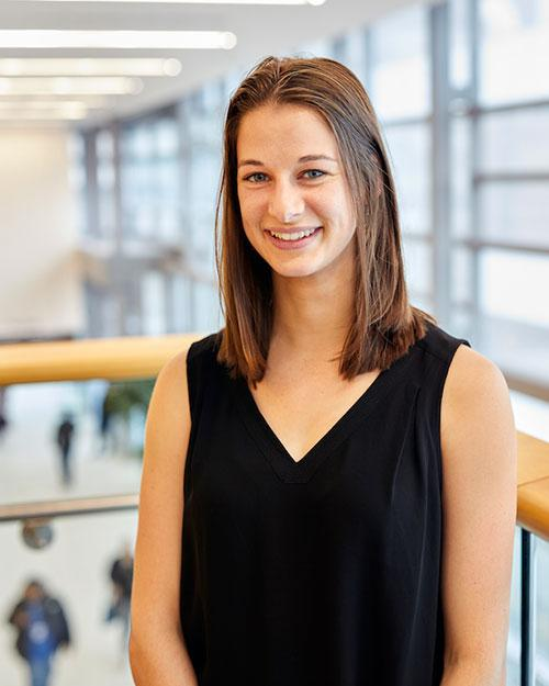 Young woman with shoulder-length brown hair in a black top, standing indoors.
