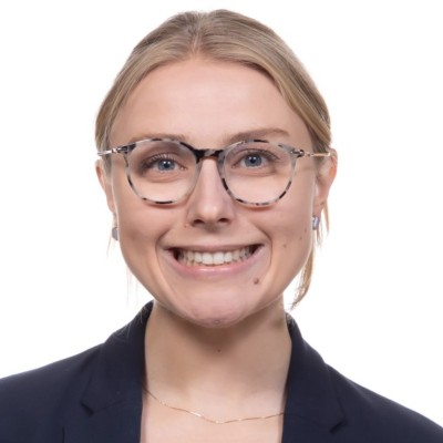 Close-up of a young woman with blonde hair, glasses, and a navy blazer against a white background.
