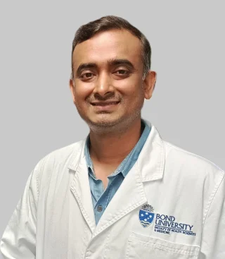 A man wearing a white lab coat standing against a light gray background.