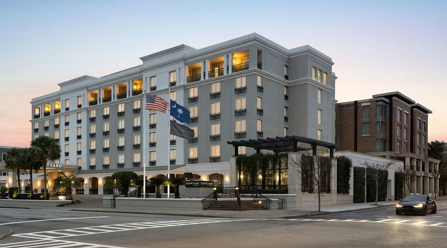 A large, modern hotel building with flags in front, located on a city street at sunset.