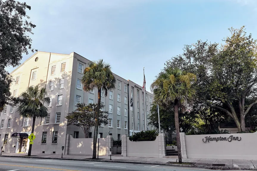 Exterior view of the Hampton Inn hotel surrounded by palm trees, with a clear sky in the background.