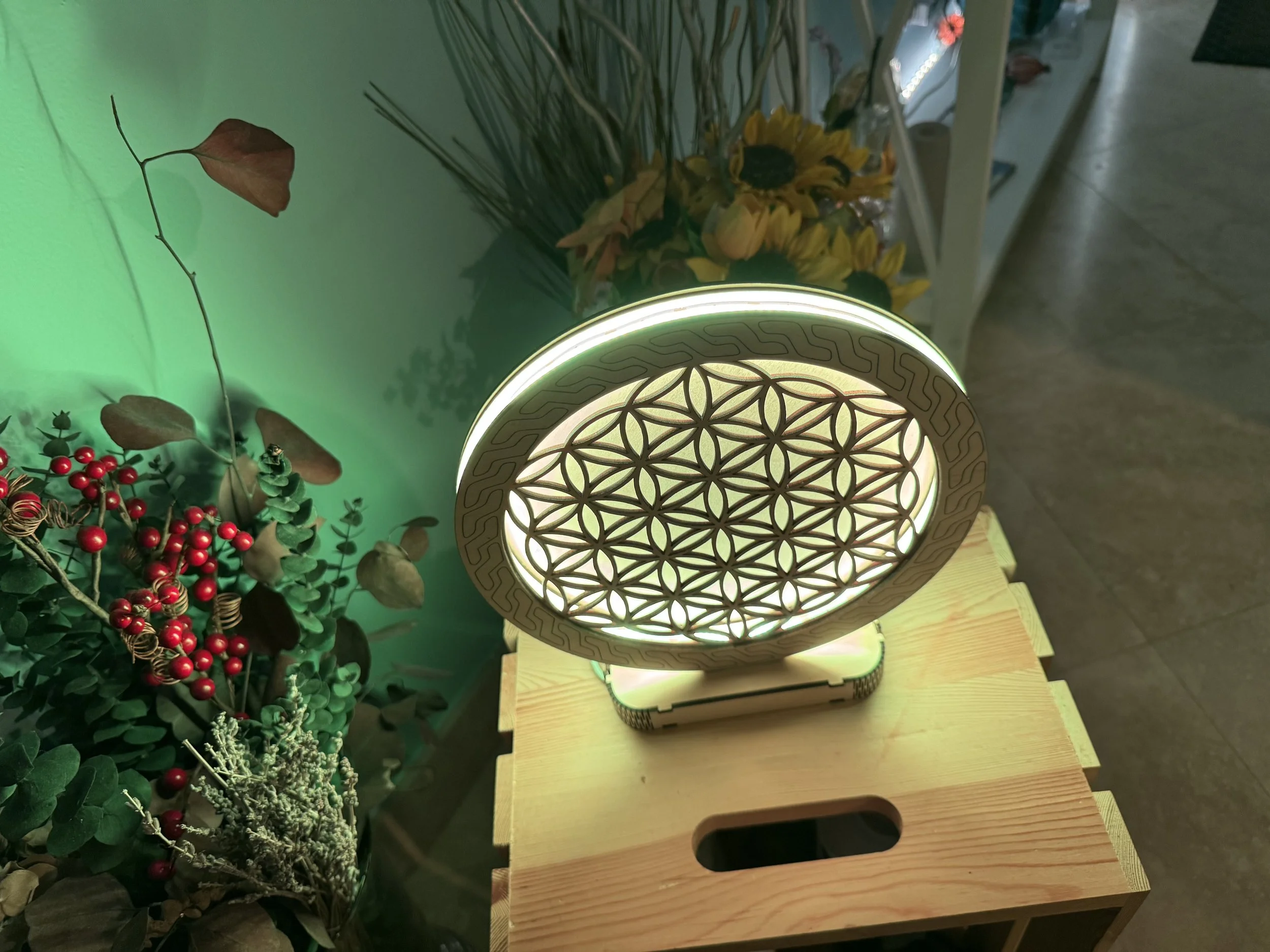 A decorative wooden object with intricate geometric patterns and LED lighting, positioned on a wooden surface next to some green plants and red berries.