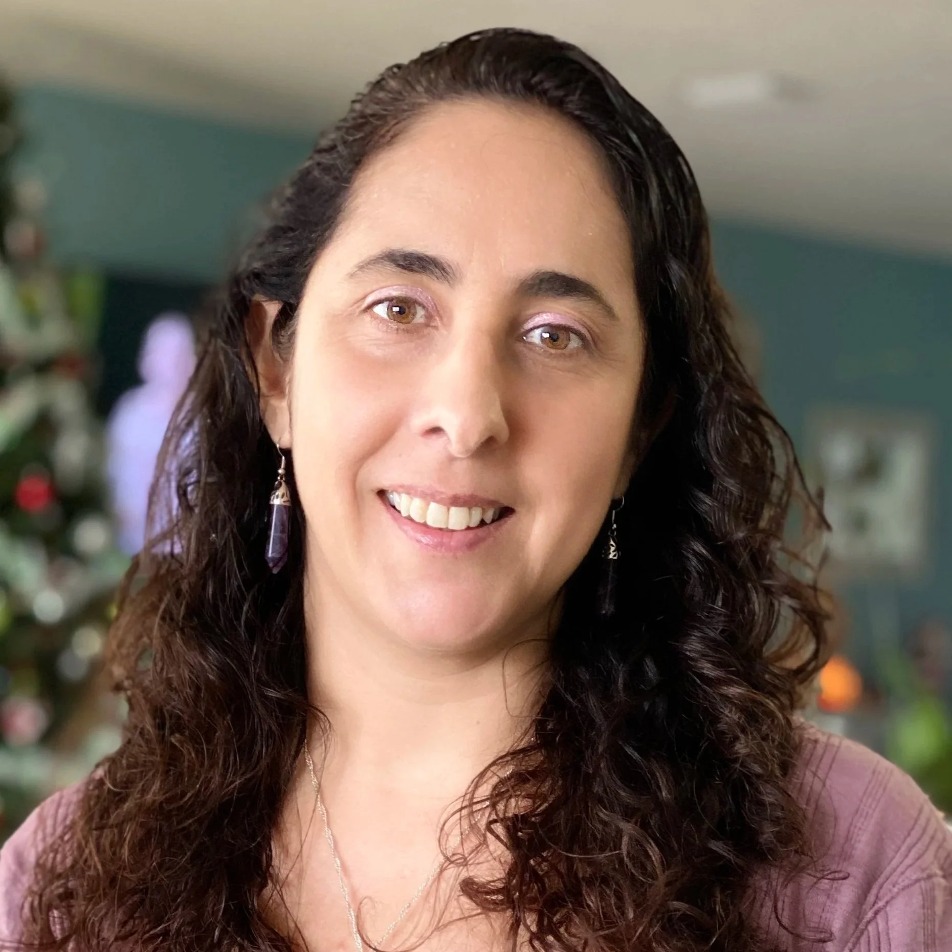 A woman with long, curly brown hair smiling indoors.
