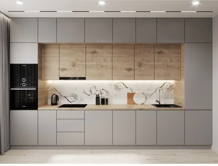 Modern kitchen with gray cabinets, wooden upper cabinets, marble backsplash, black built-in oven, kettle, and sink.