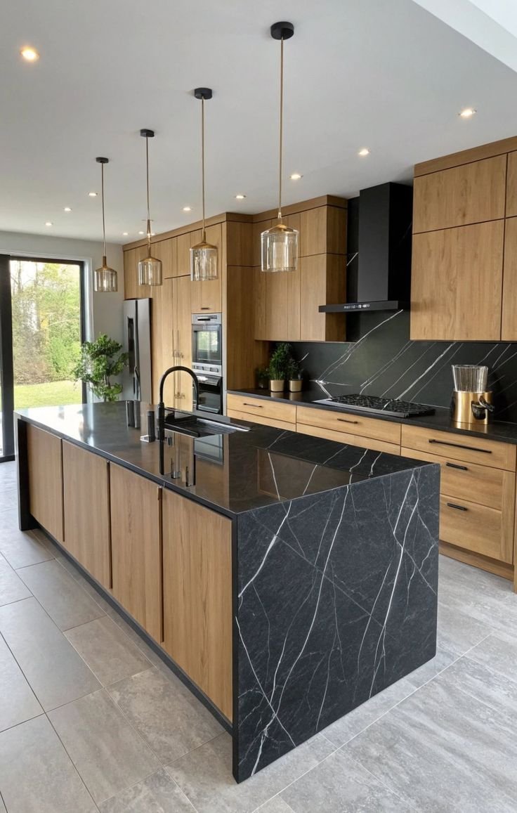 Modern kitchen with black marble island, wooden cabinets, and black appliances, pendant lights, and sliding glass door to outside.