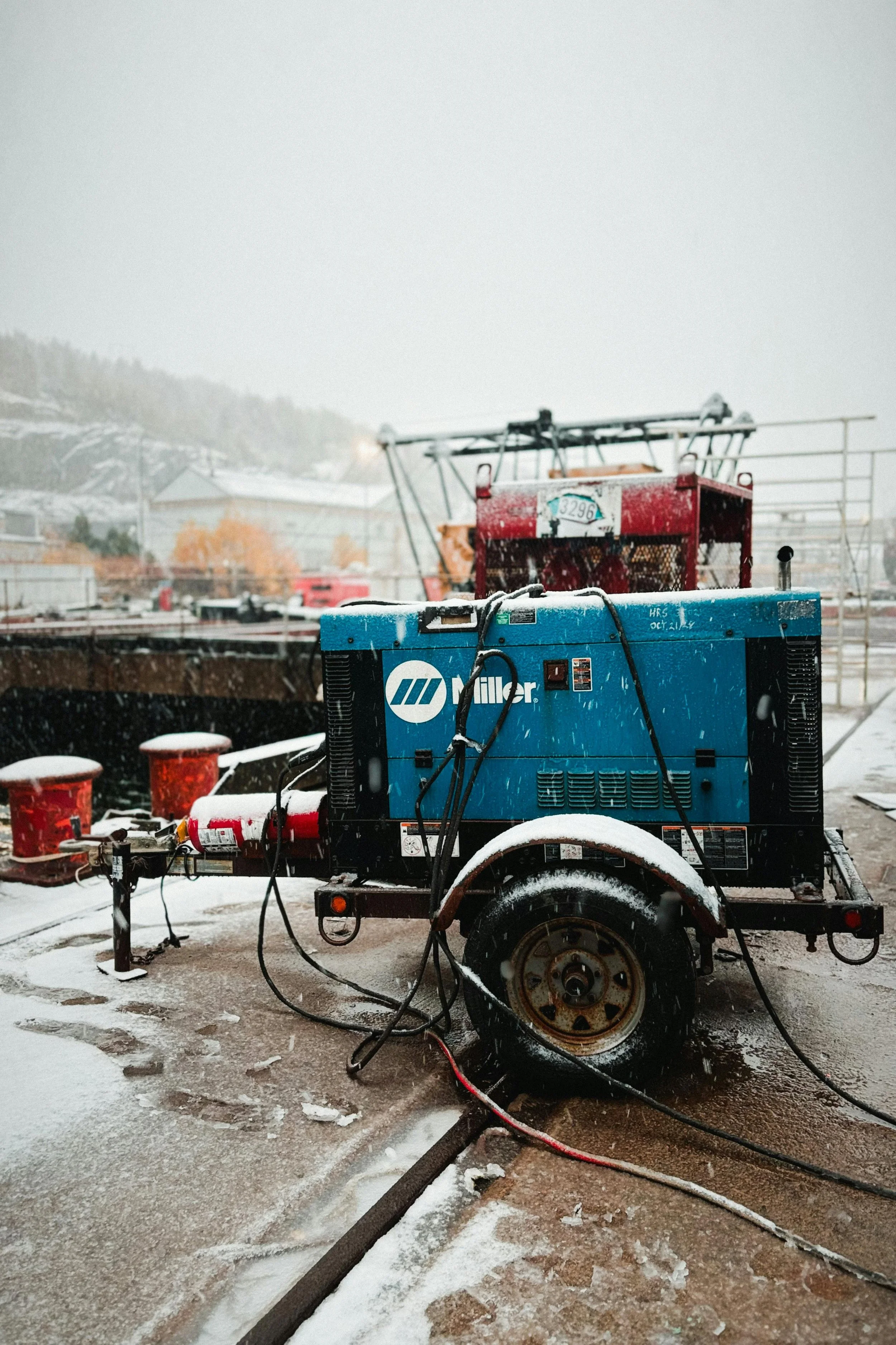 A Miller portable generator on a snow-covered dock, with snow falling and industrial equipment in the background.