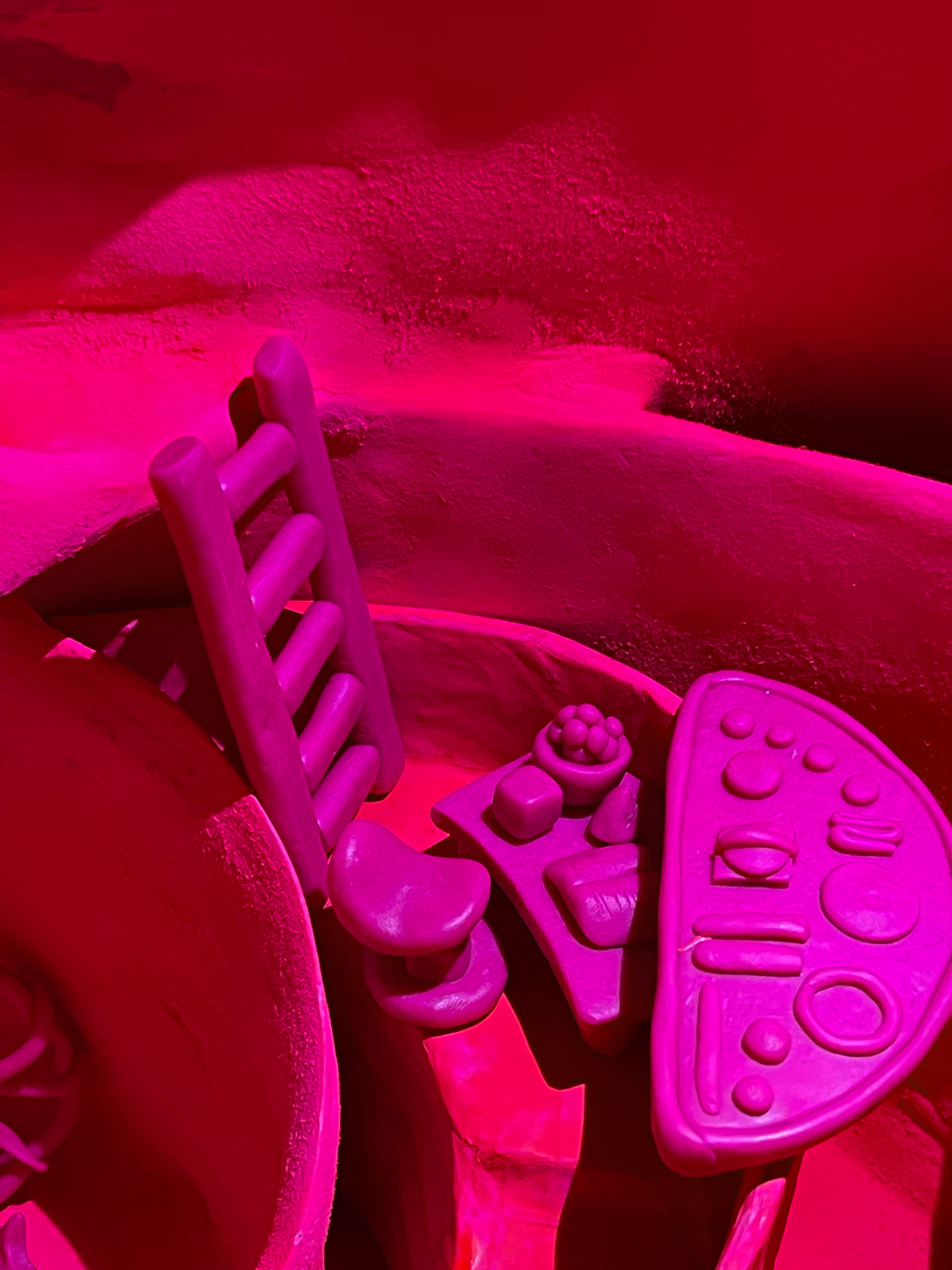 Pink plastic toy kitchen set including a chair, pizzas, and various pretend food and utensils arranged on a small table.