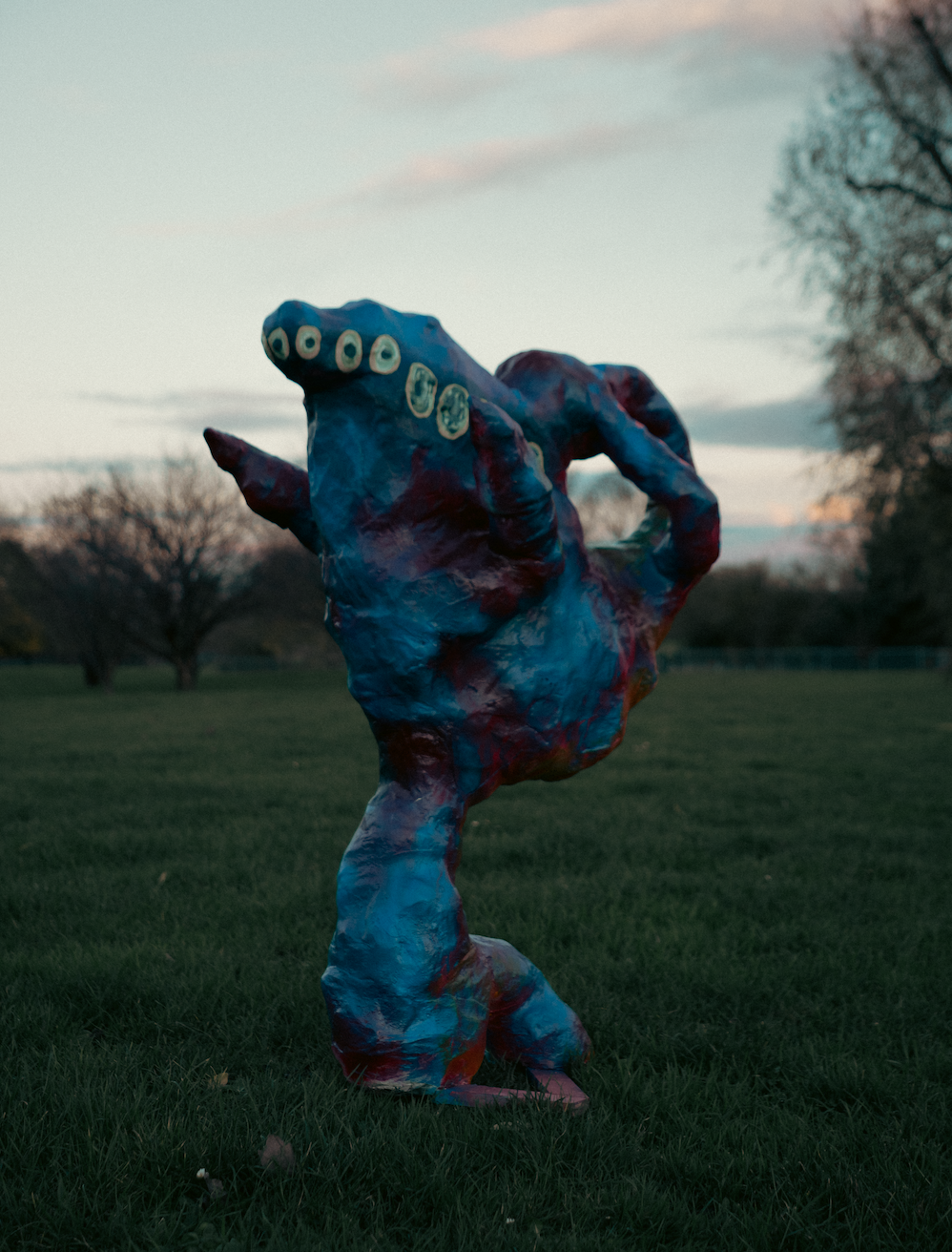 A colorful sculpture of a creature with multiple eyes on a grassy field during sunset.
