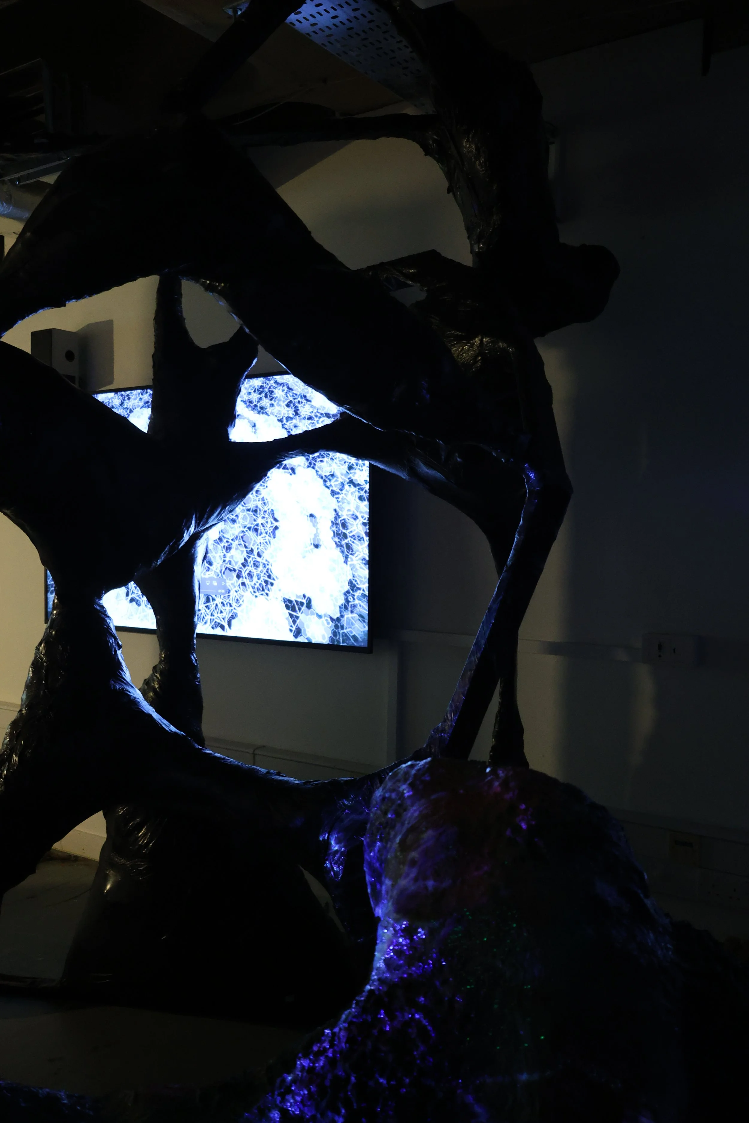Dark abstract sculpture in front of a screen displaying a digital pattern with blue and white colors.