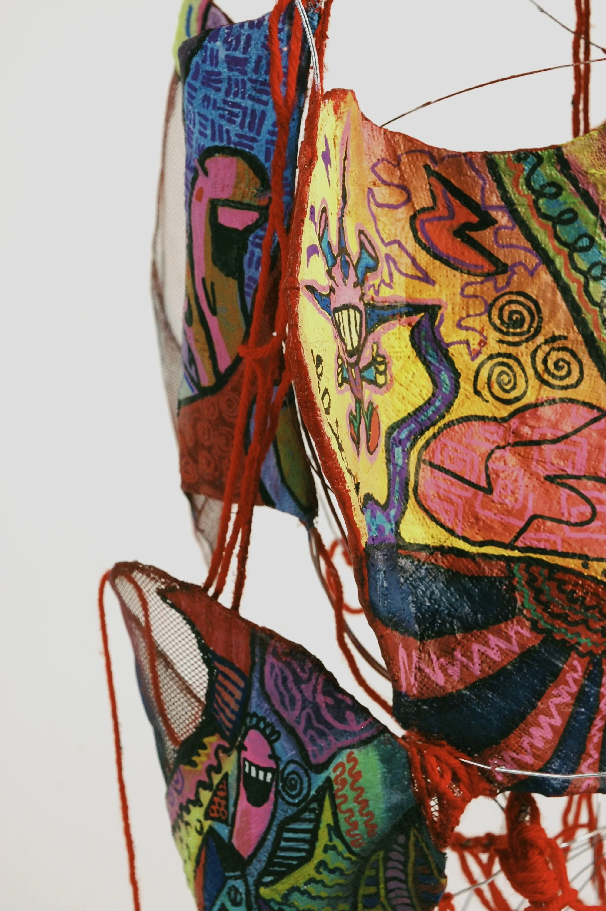 Colorful fabric art pieces hanging with abstract and cartoon-like designs, featuring bright colors and patterns.