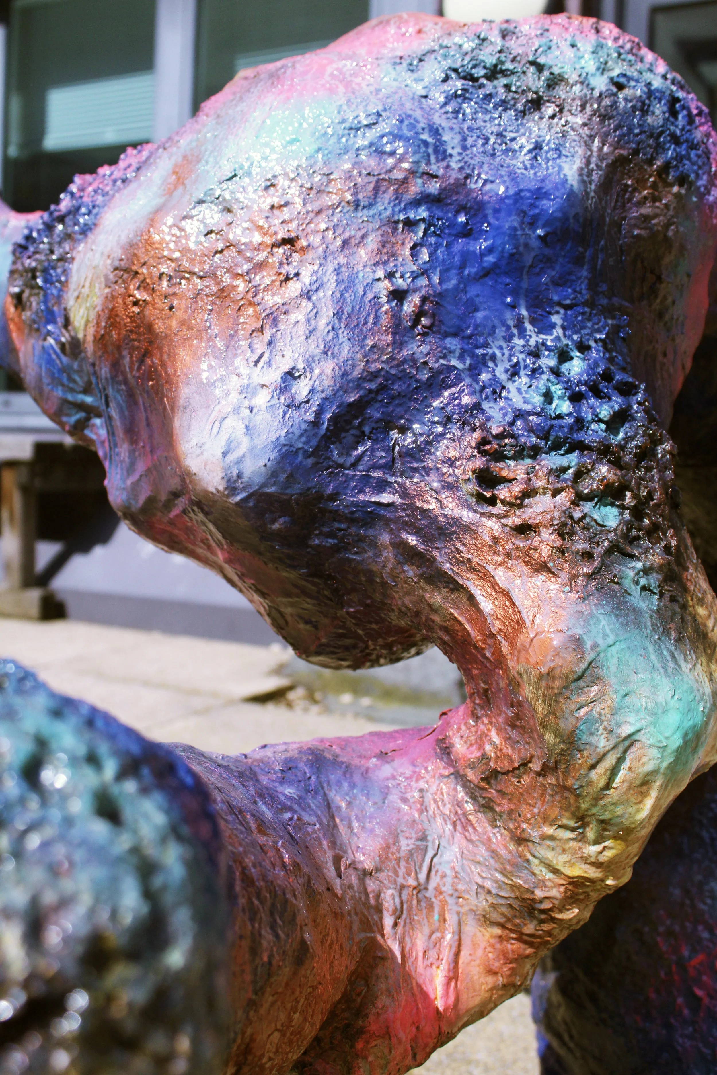 Close-up of a colorful, textured sculpture of a dog, painted with bright, iridescent colors including pink, blue, purple, and green.