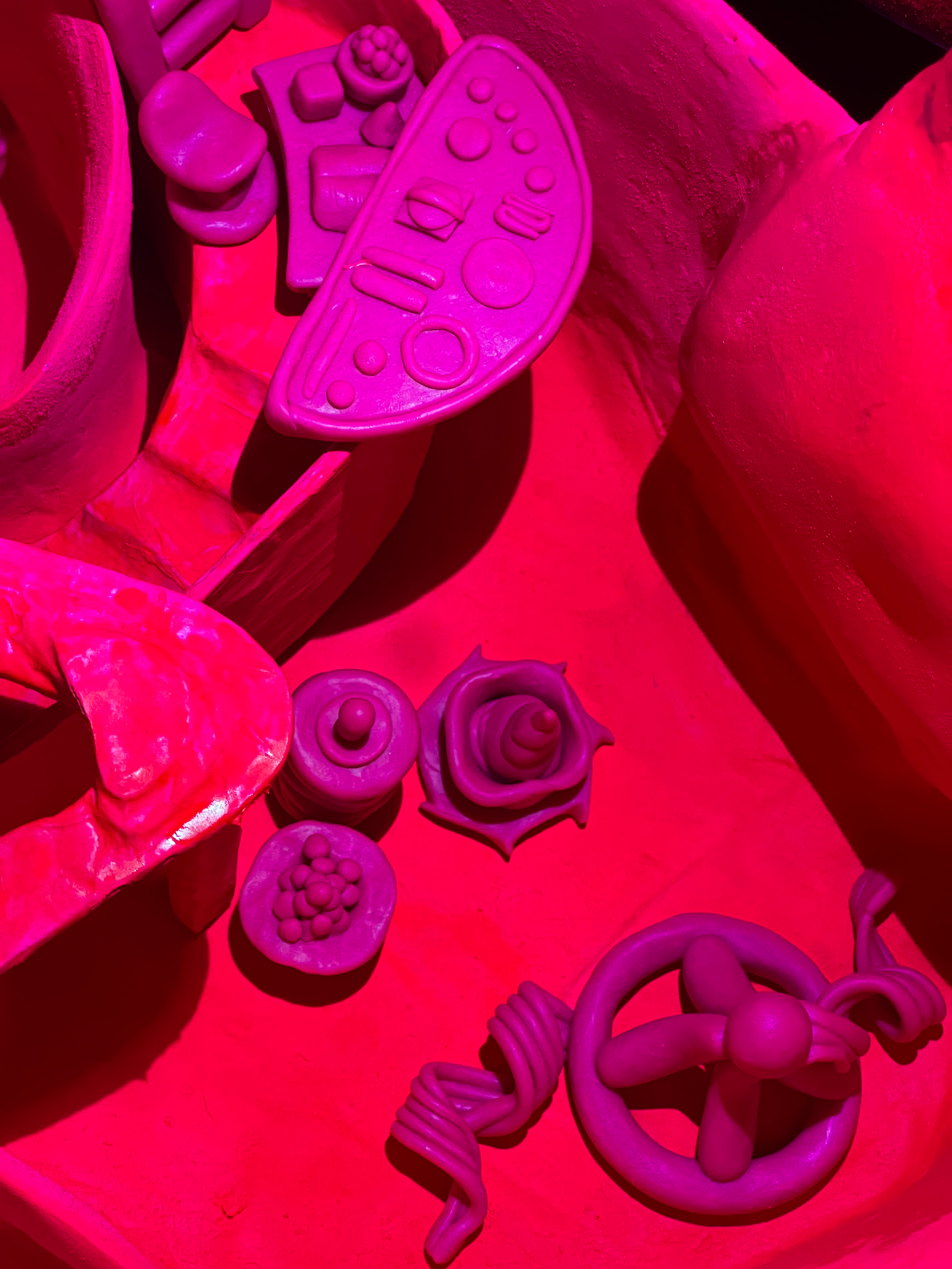 Collection of pink plastic toys resembling food and kitchen items, including a remote control, a rose, sliced fruit, and a star-shaped item.