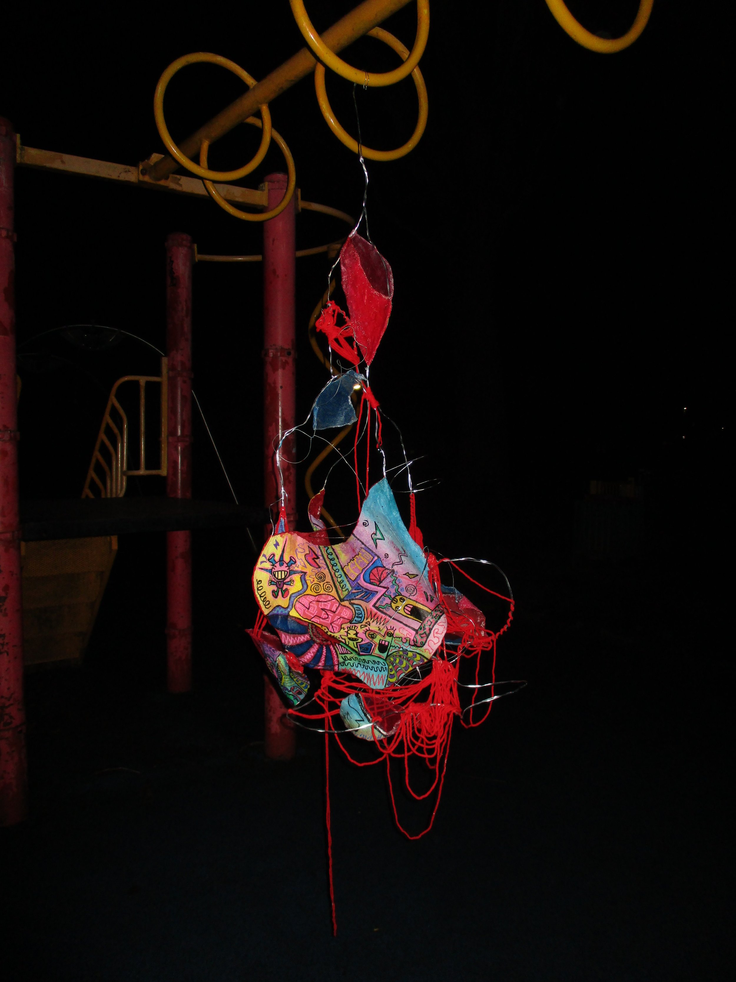 Colorful paper kite with illustrations hanging in a dark playground.