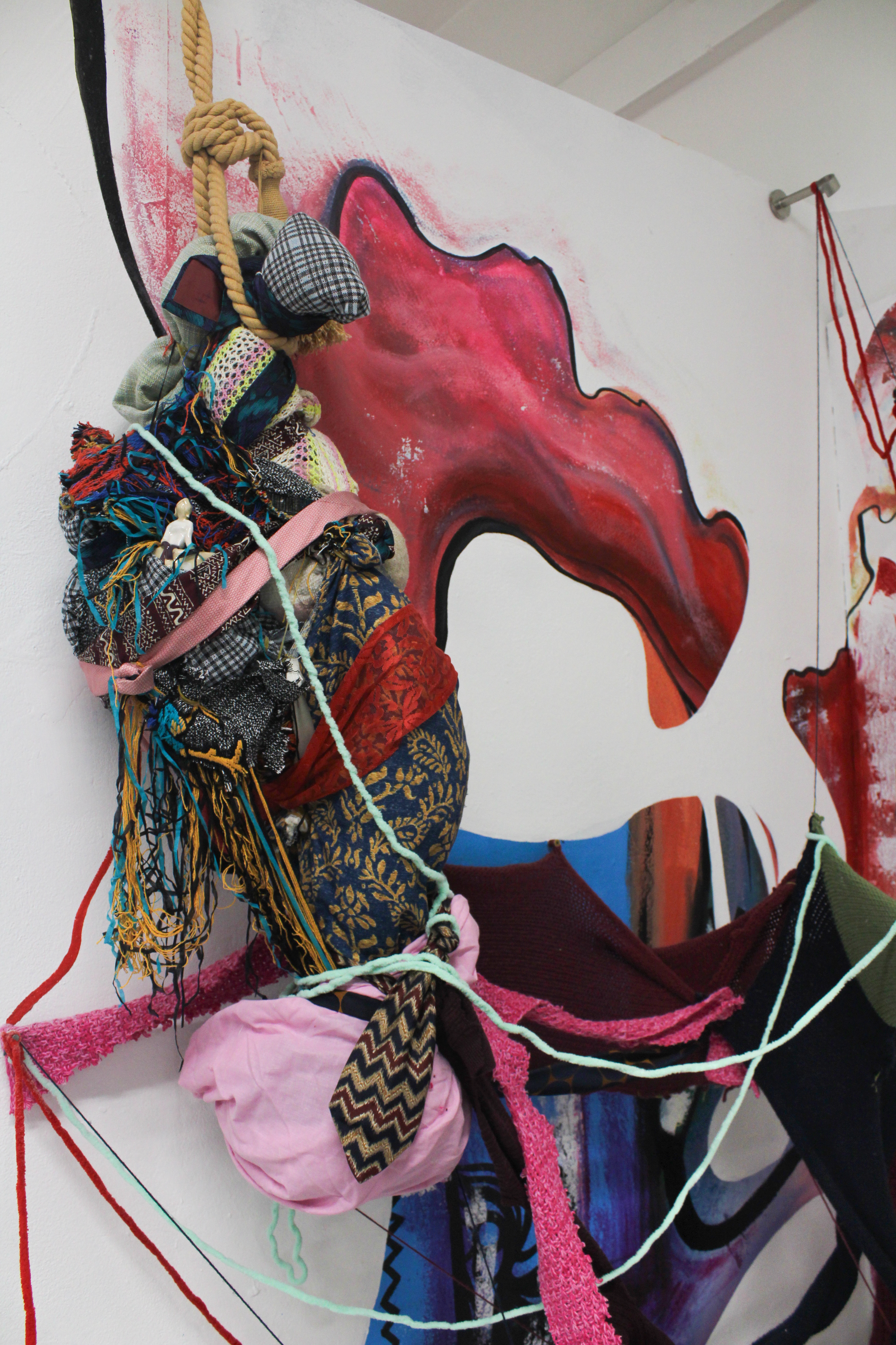 Mixed media art installation featuring textiles, yarn, and fabric sculptures in front of a colorful abstract mural.