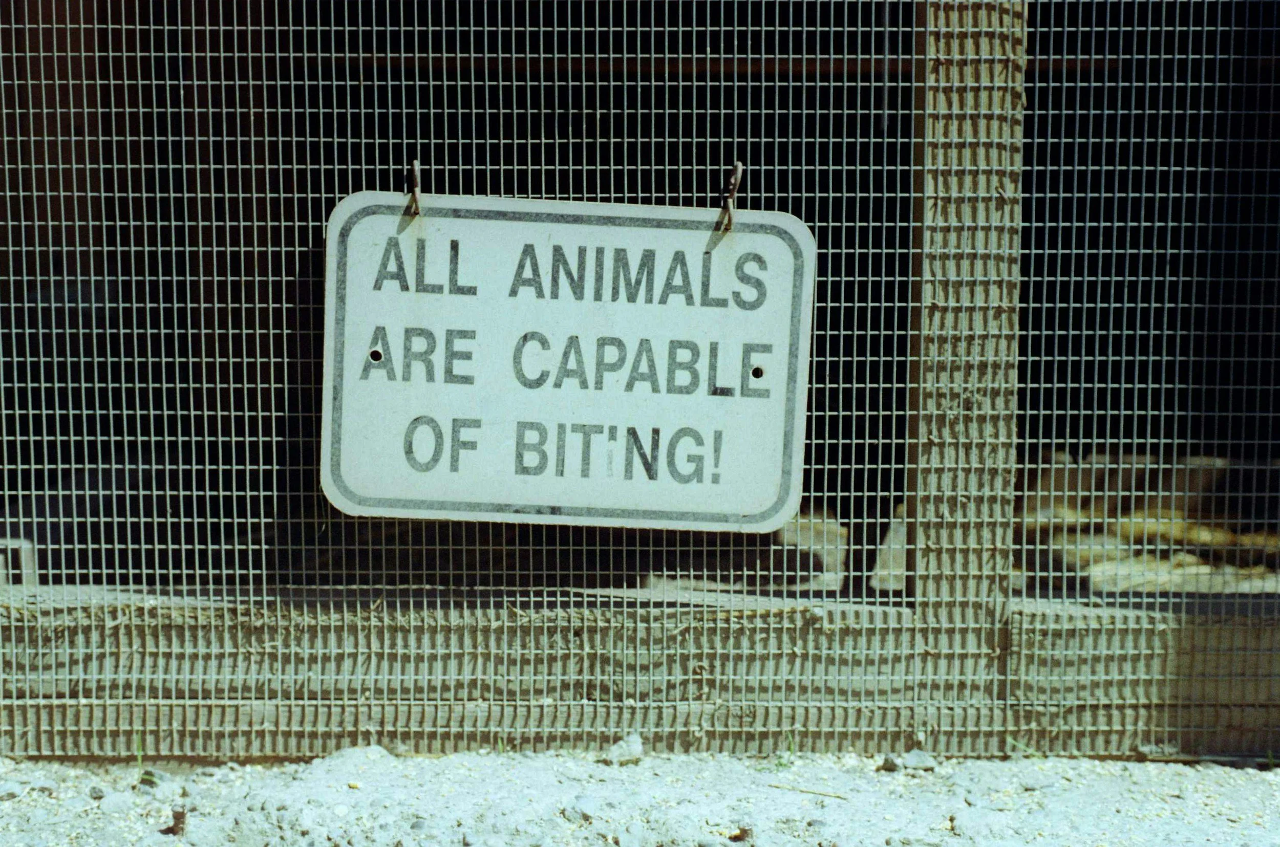 A metal fence with a sign that reads 'All animals are capable of biting!' in front of an animal enclosure.